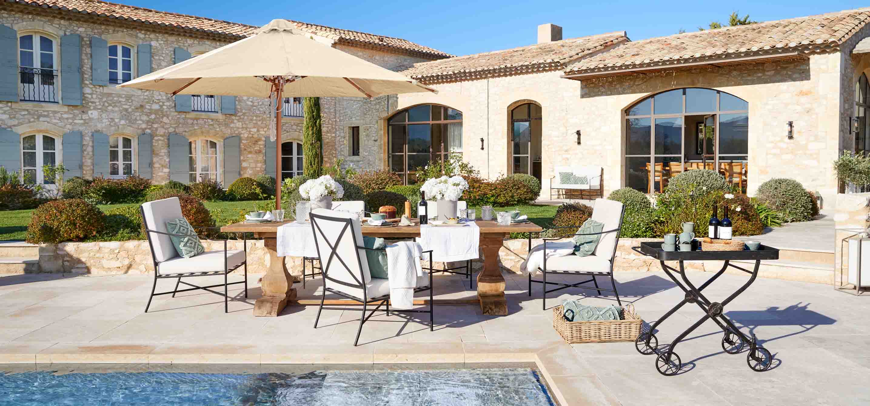 Conjunto de muebles de jardín con mesa de madera y cojines crema junto a la piscina en estilo rústico