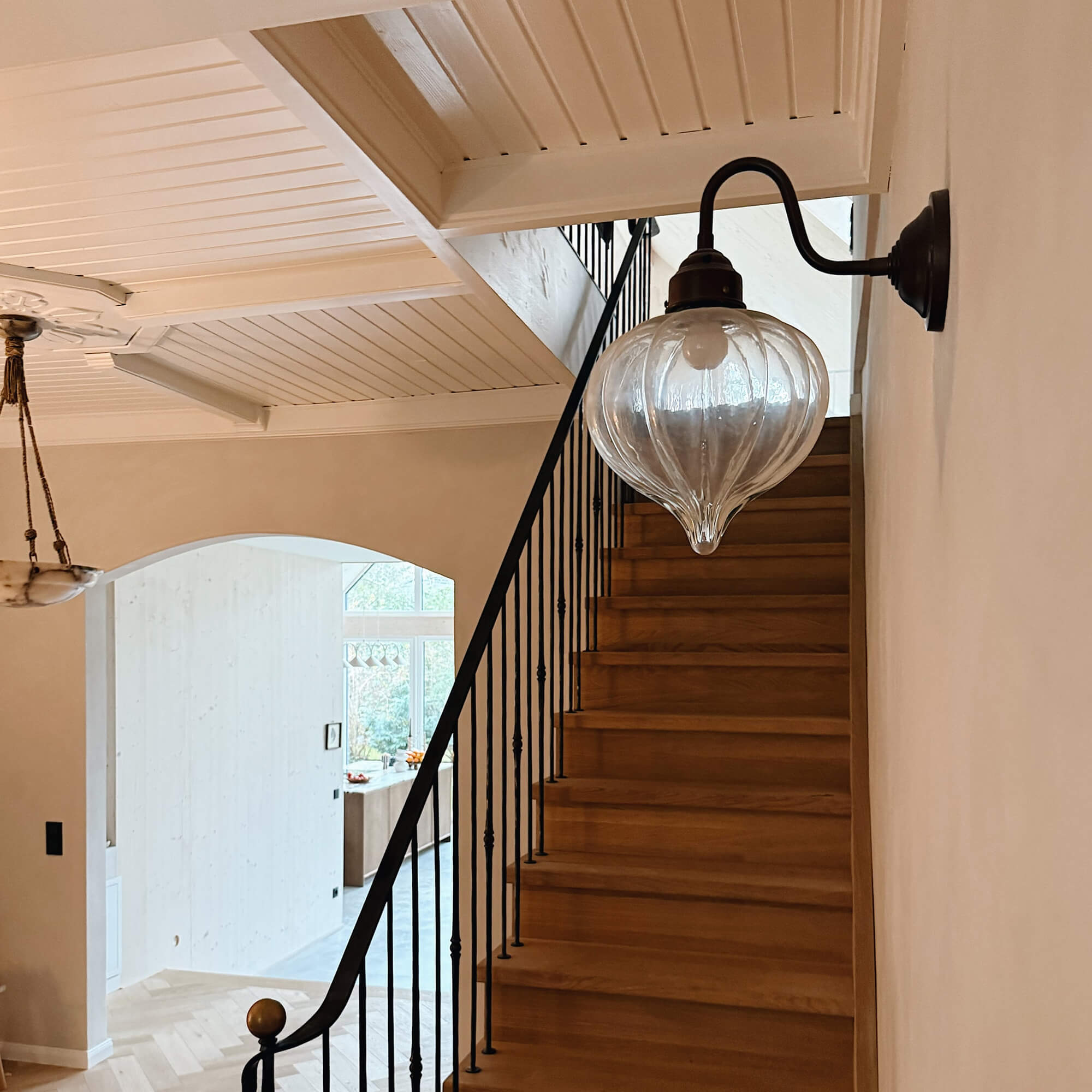 Aplique de pared de vidrio con brazo metálico negro sobre escalera de madera en interior luminoso