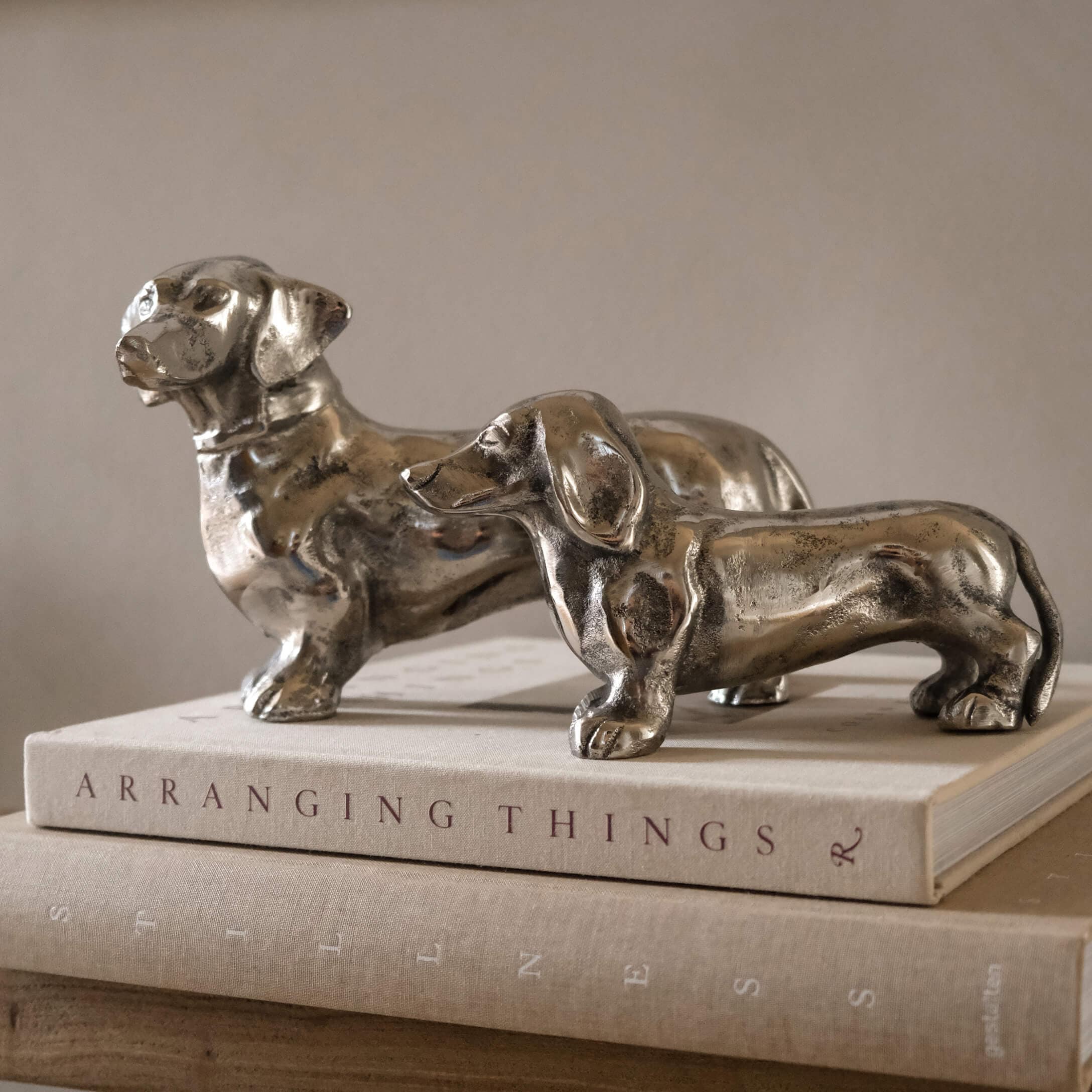 Dos figuras de teckel de metal plateado sobre libros, decoración para interiores