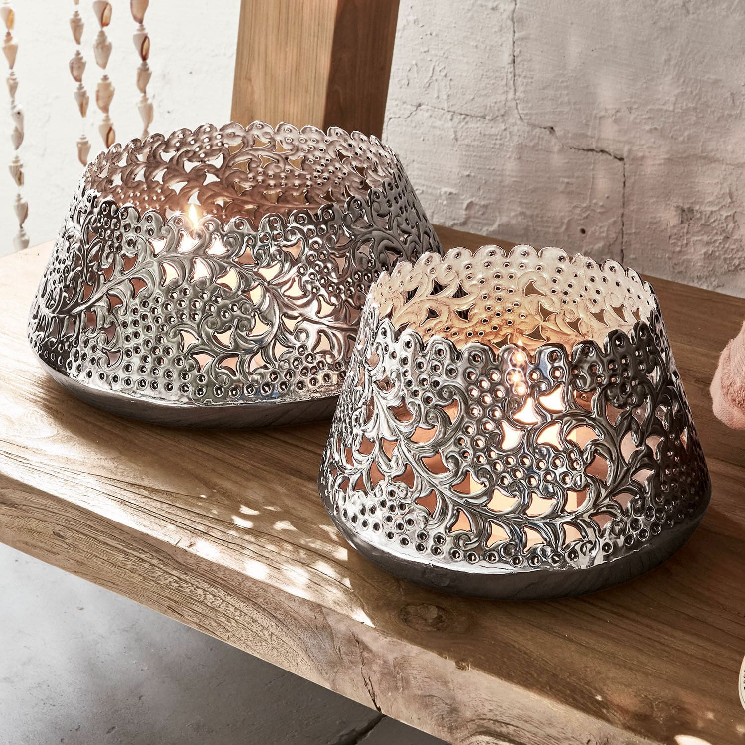 Set de 2 linternas Brebotte Dos portavelas de metal calado en color plateado sobre mesa de madera, iluminación decorativa interior
