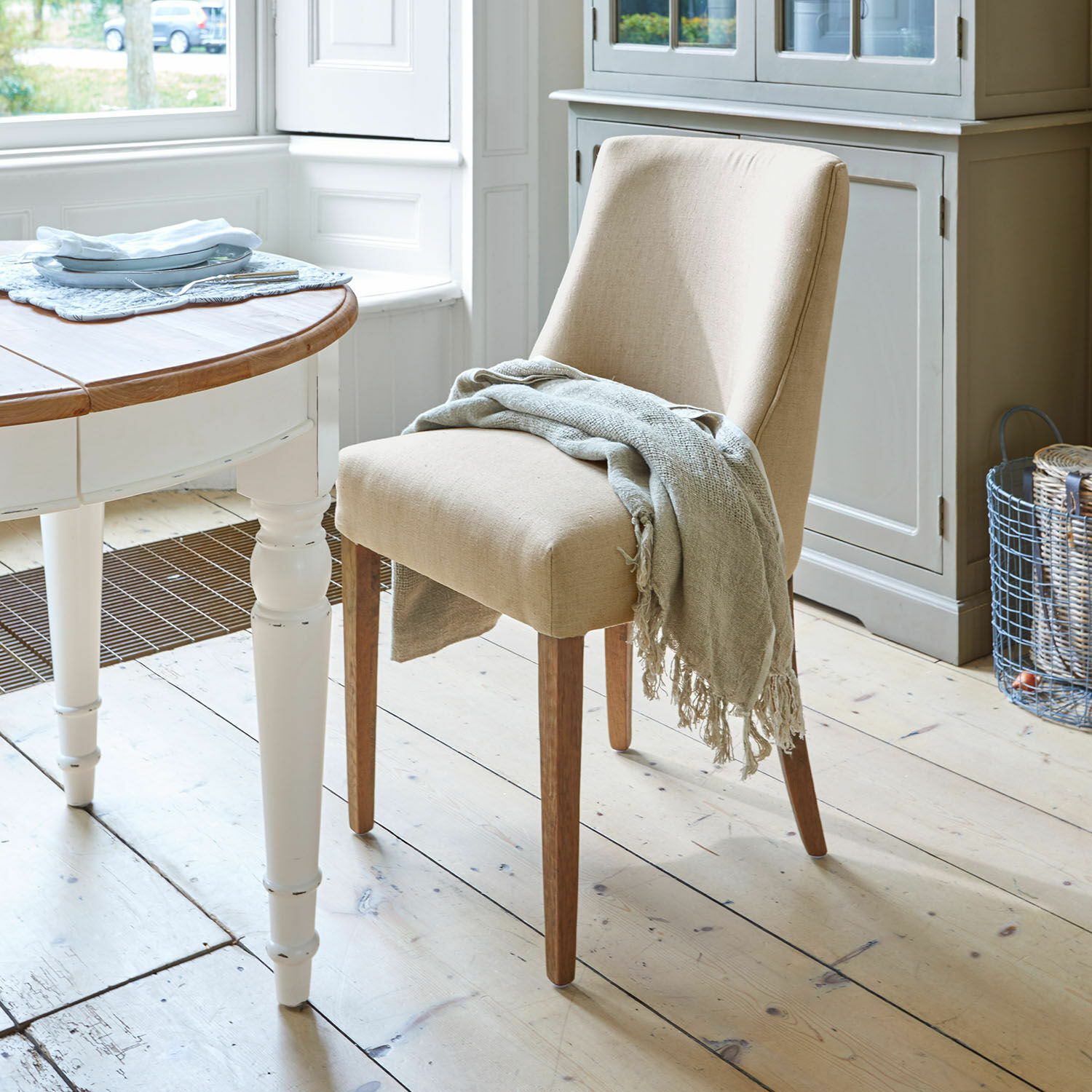 Silla Opirel Silla tapizada beige con patas de madera y manta gris en comedor luminoso