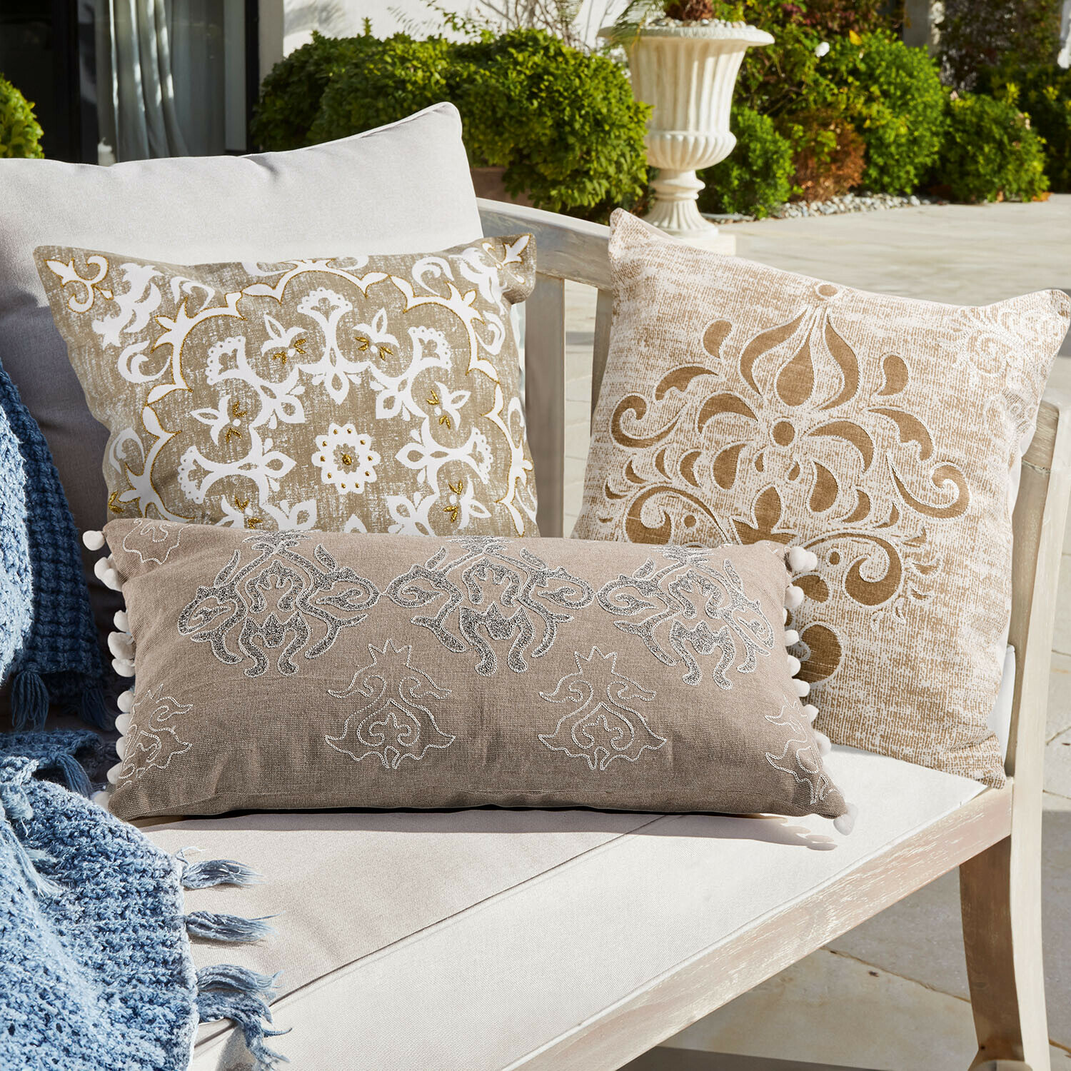 Set de 3 fundas de cojín Emelin Conjunto de cojines decorativos beige y blanco con patrones sobre sofá claro en terraza