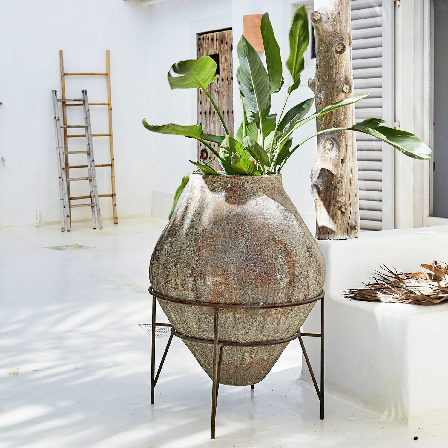 Maceta grande de piedra sobre soporte metálico con planta verde en interior claro y minimalista
