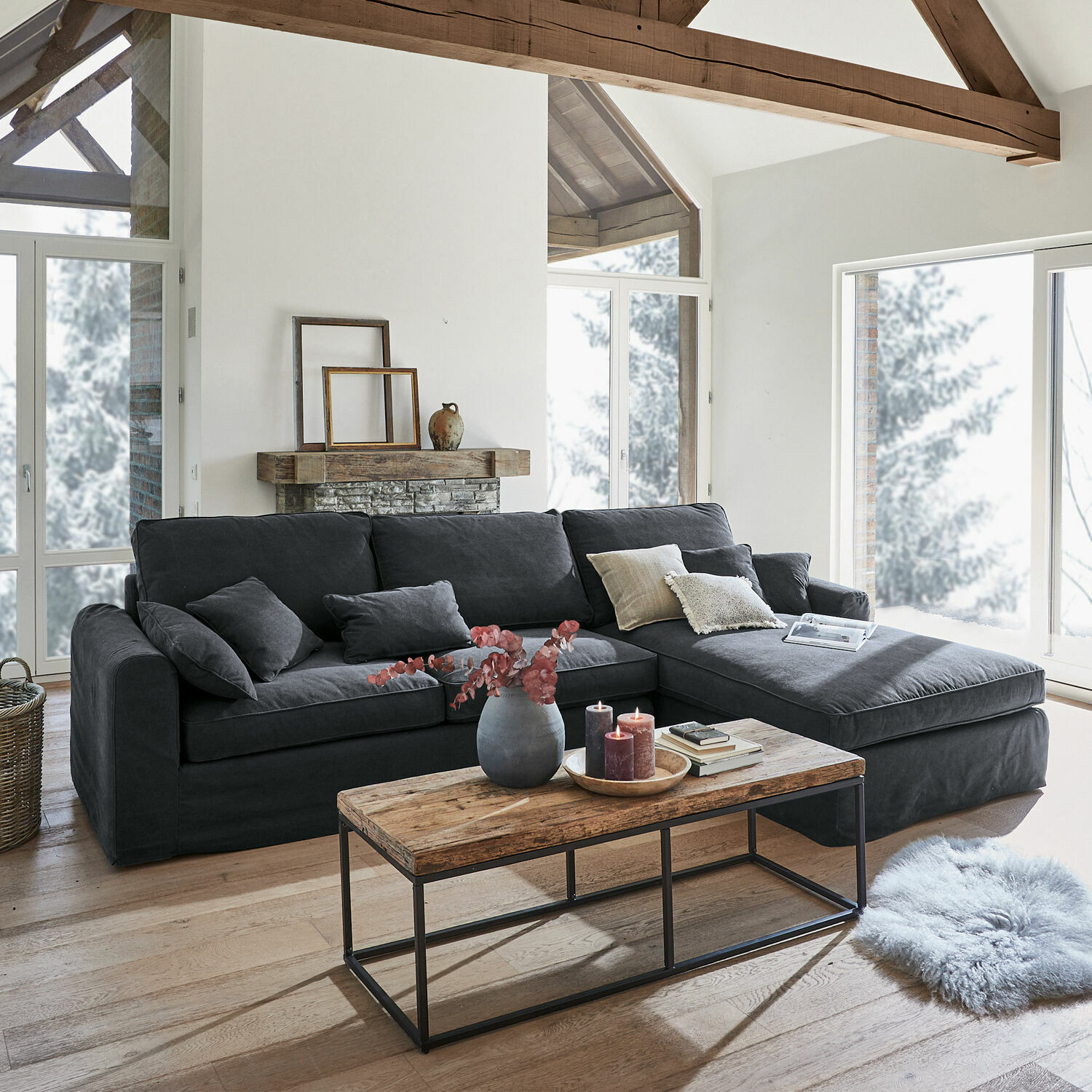 Sofá Seaford Sofá esquinero gris de tela en sala moderna con mesa de madera y grandes ventanas
