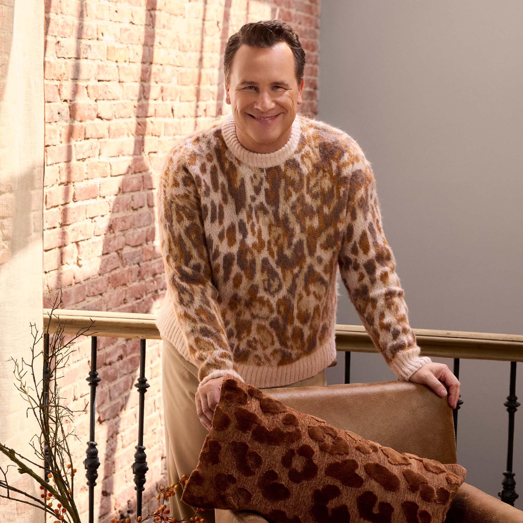 Hombre con suéter suave de estampado de leopardo marrón claro junto a pared de ladrillo