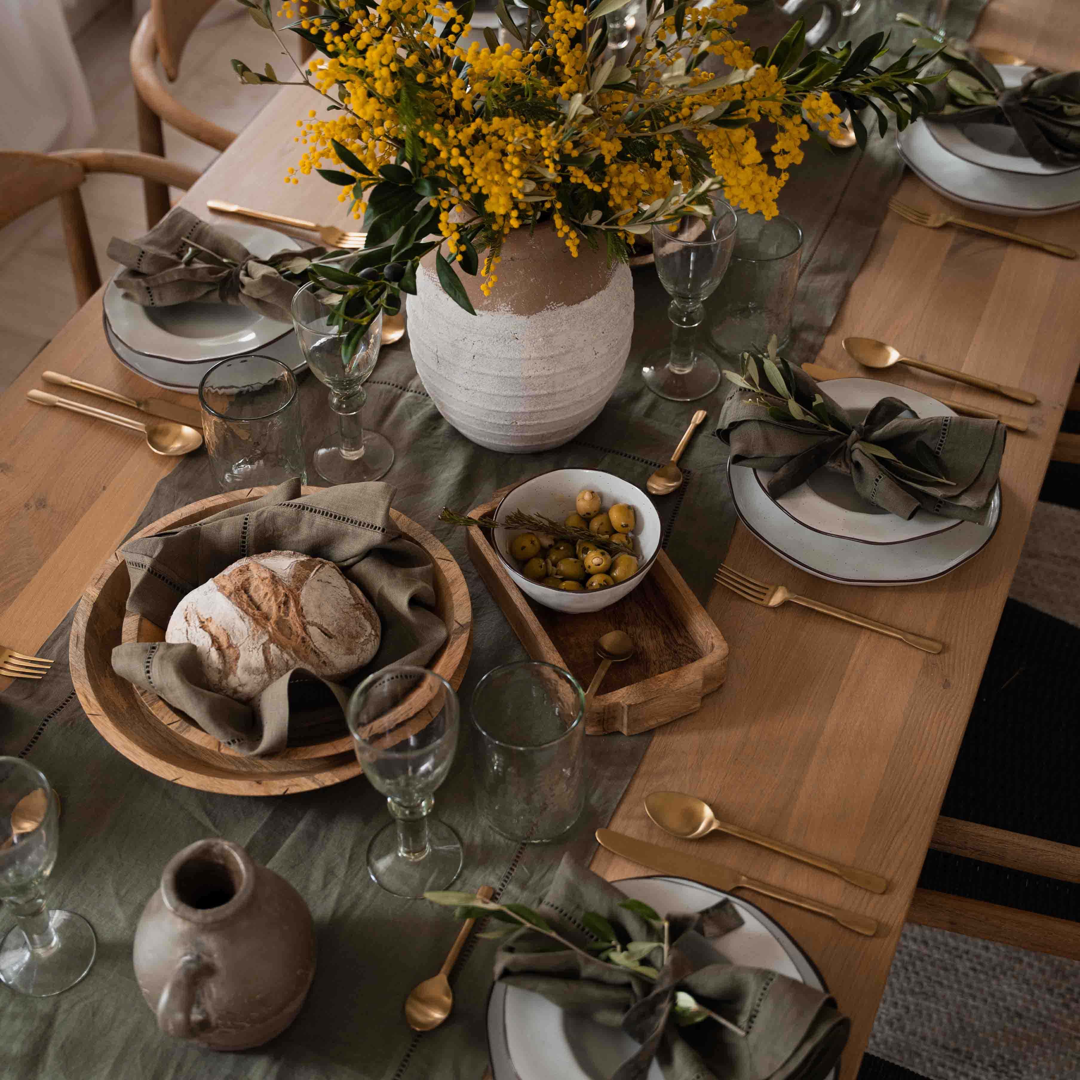 Mesa rústica de madera con vajilla blanca, servilletas verdes y ramo de flores amarillas en jarrón de barro