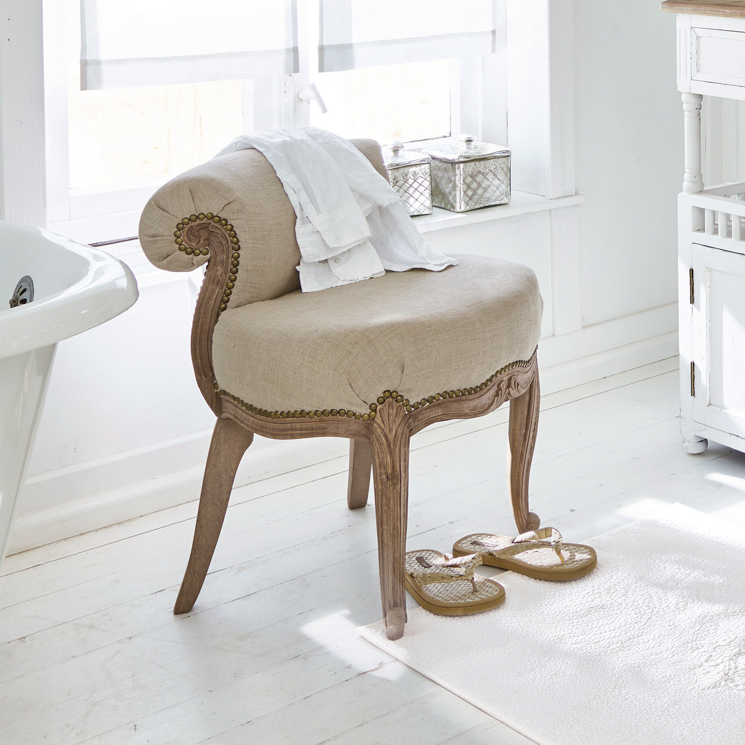 Sillón Rivel Sillón beige tapizado con marco de madera tallada en baño luminoso