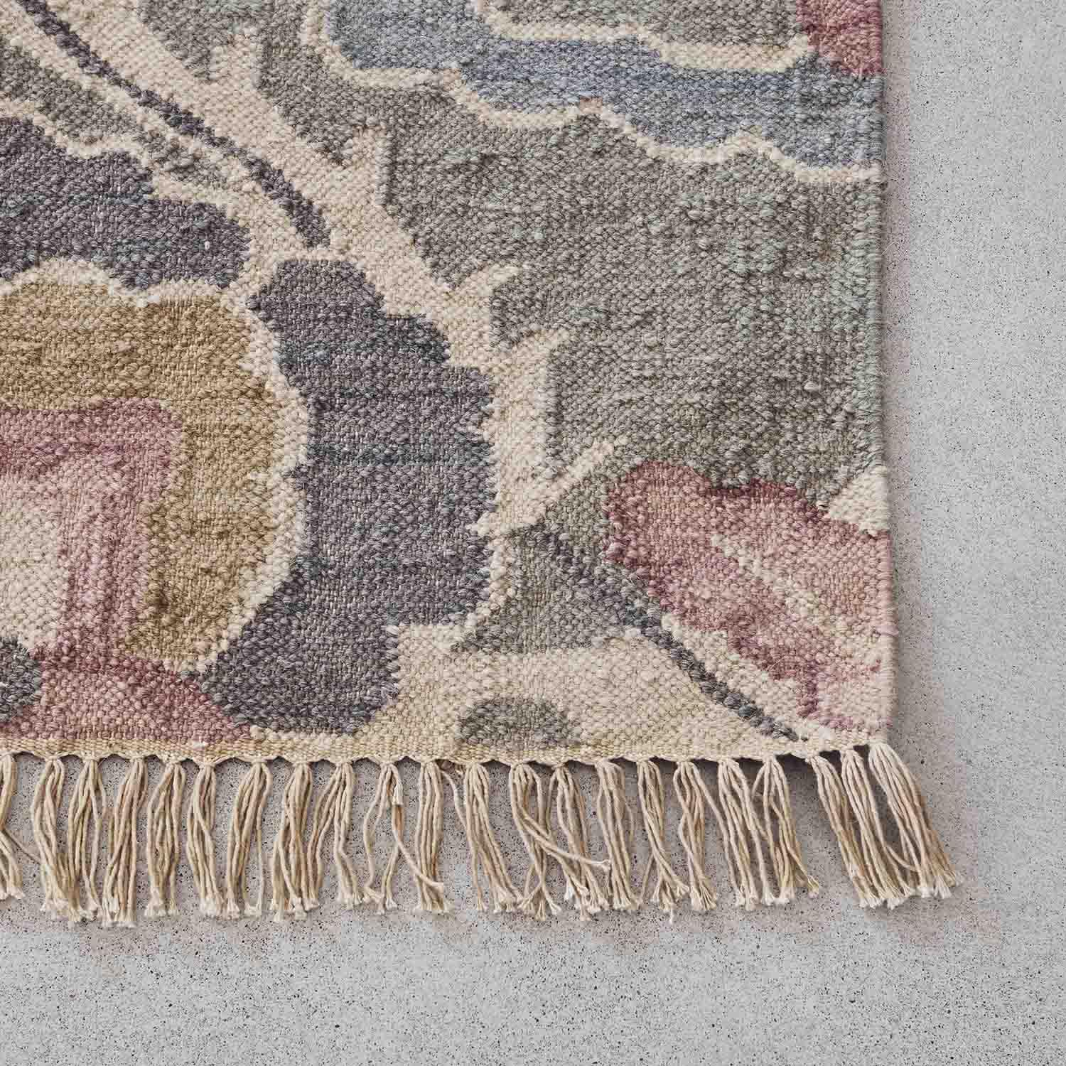 Alfombra con flecos en tonos pastel rosa, gris y beige, material suave con diseño floral decorativo