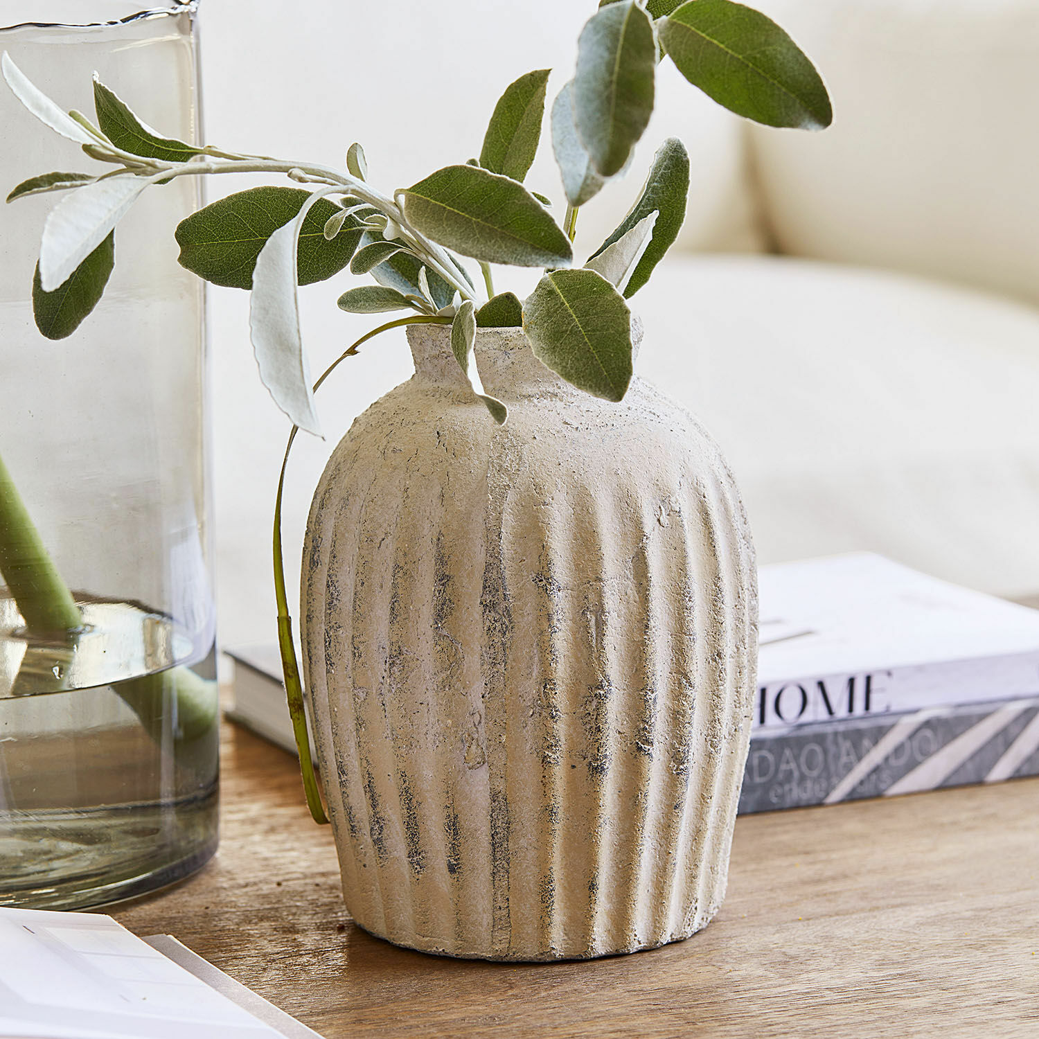Jarrón de cerámica beige con textura y hojas verdes sobre mesa de madera para decoración interior