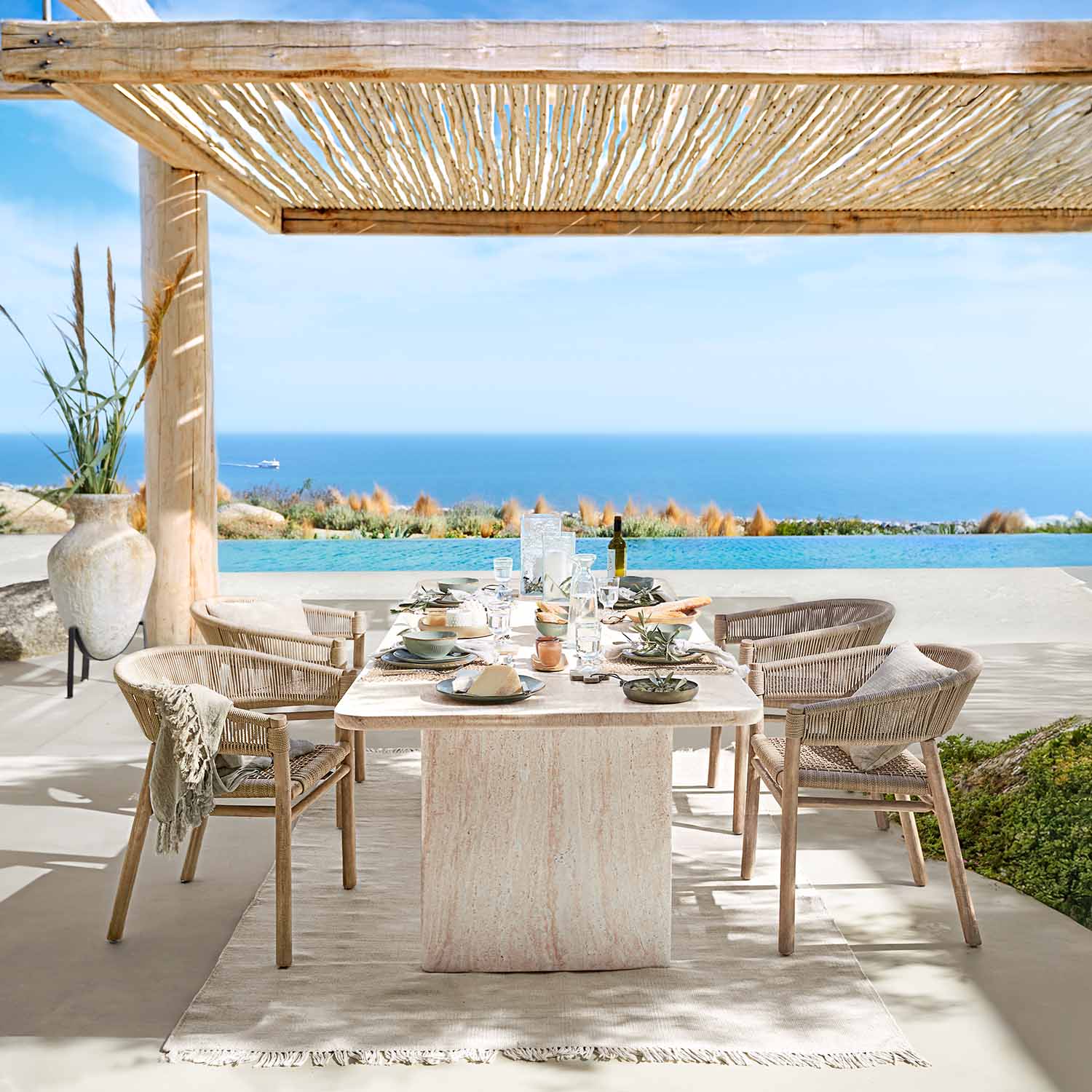Comedor exterior con mesa de piedra natural y sillas de mimbre con vistas al mar