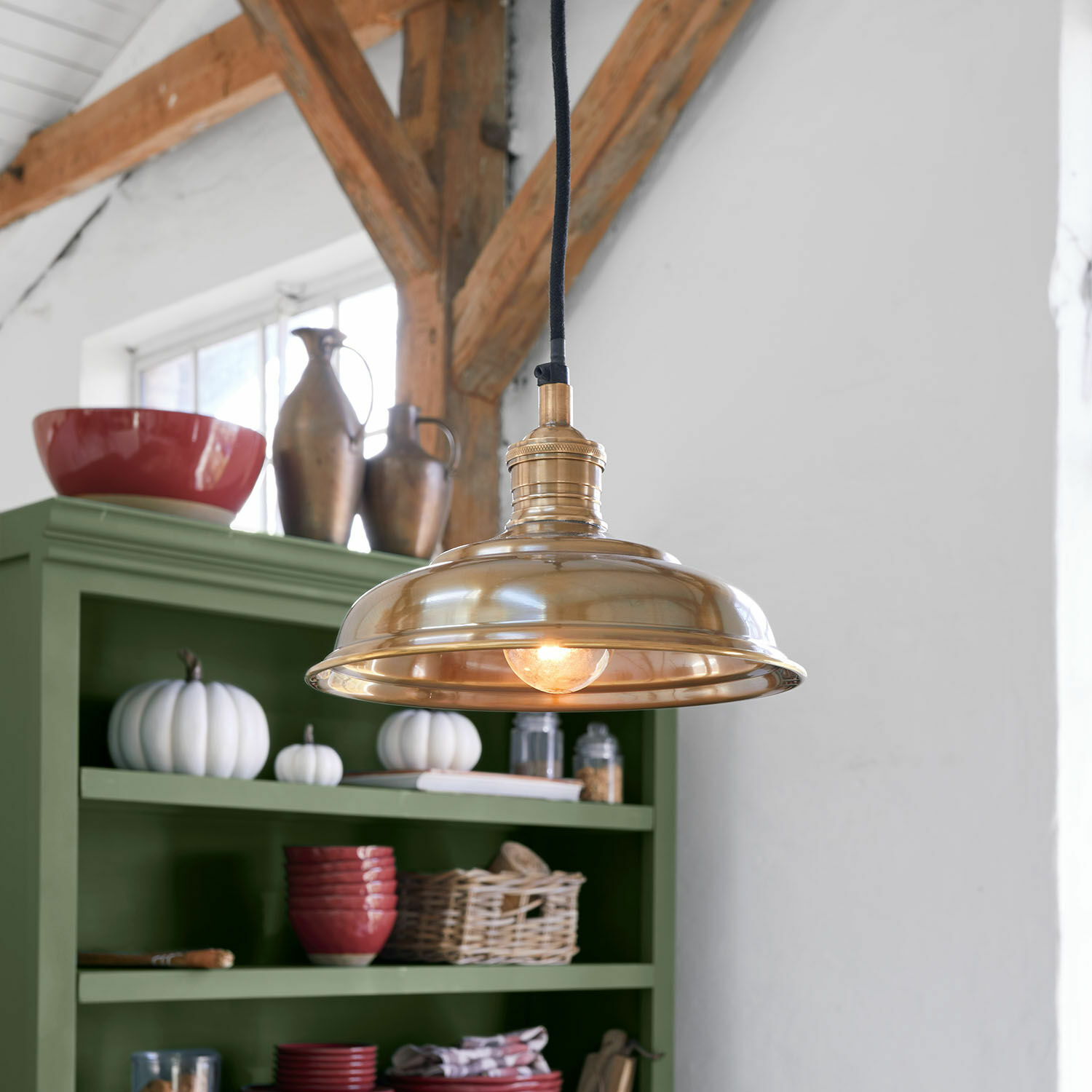 Lámpara colgante de latón con cable negro en cocina rústica con estantería verde y decoraciones