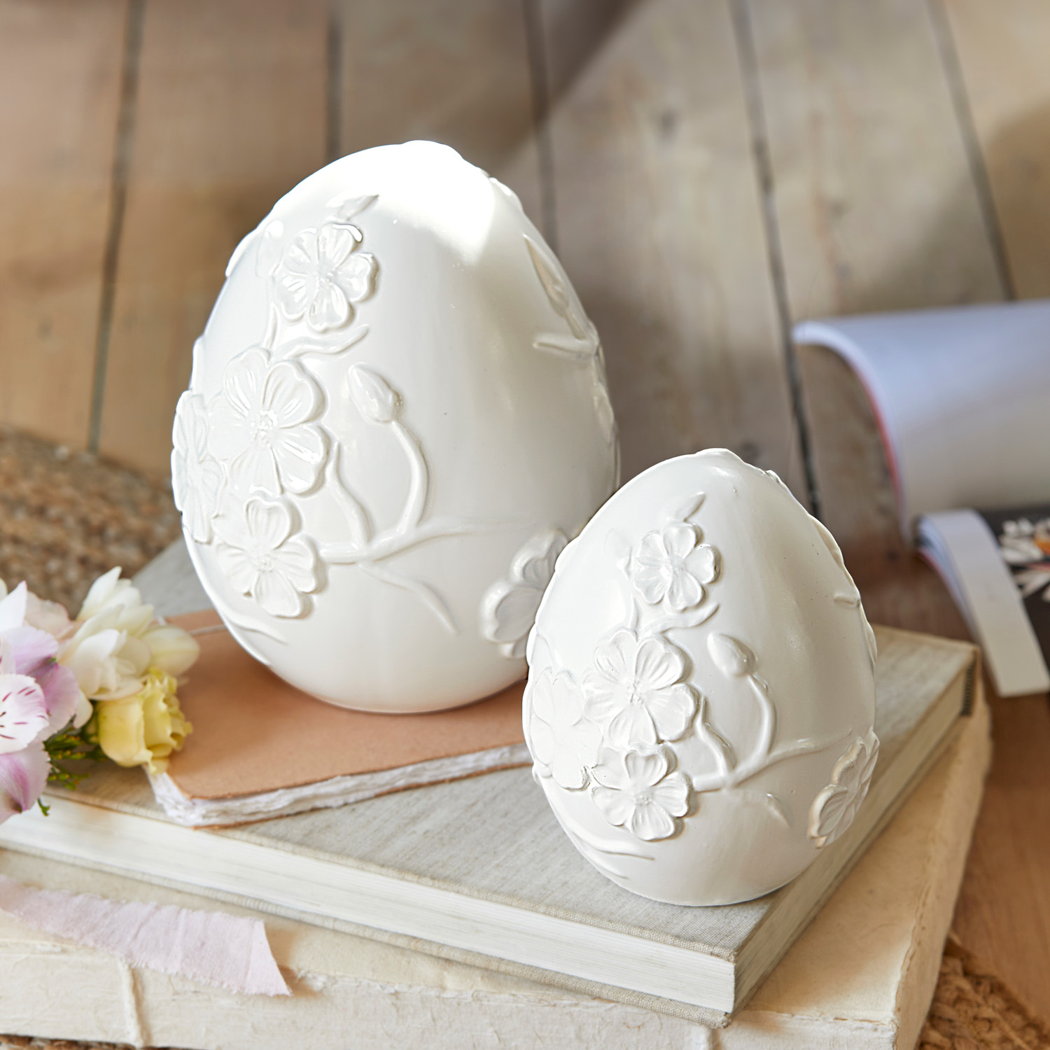 Huevos decorativos de cerámica blanca con relieve floral sobre libros, decoración primaveral