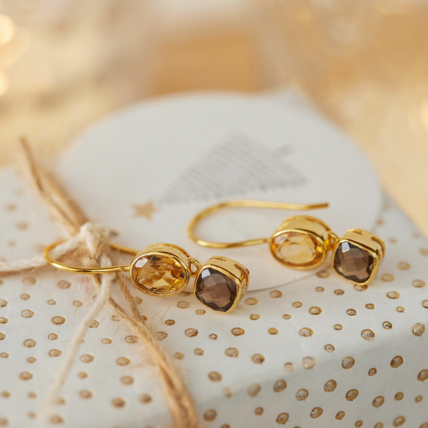 Pendientes Ovique Pendientes dorados con piedras facetadas marrones sobre papel de regalo decorativo