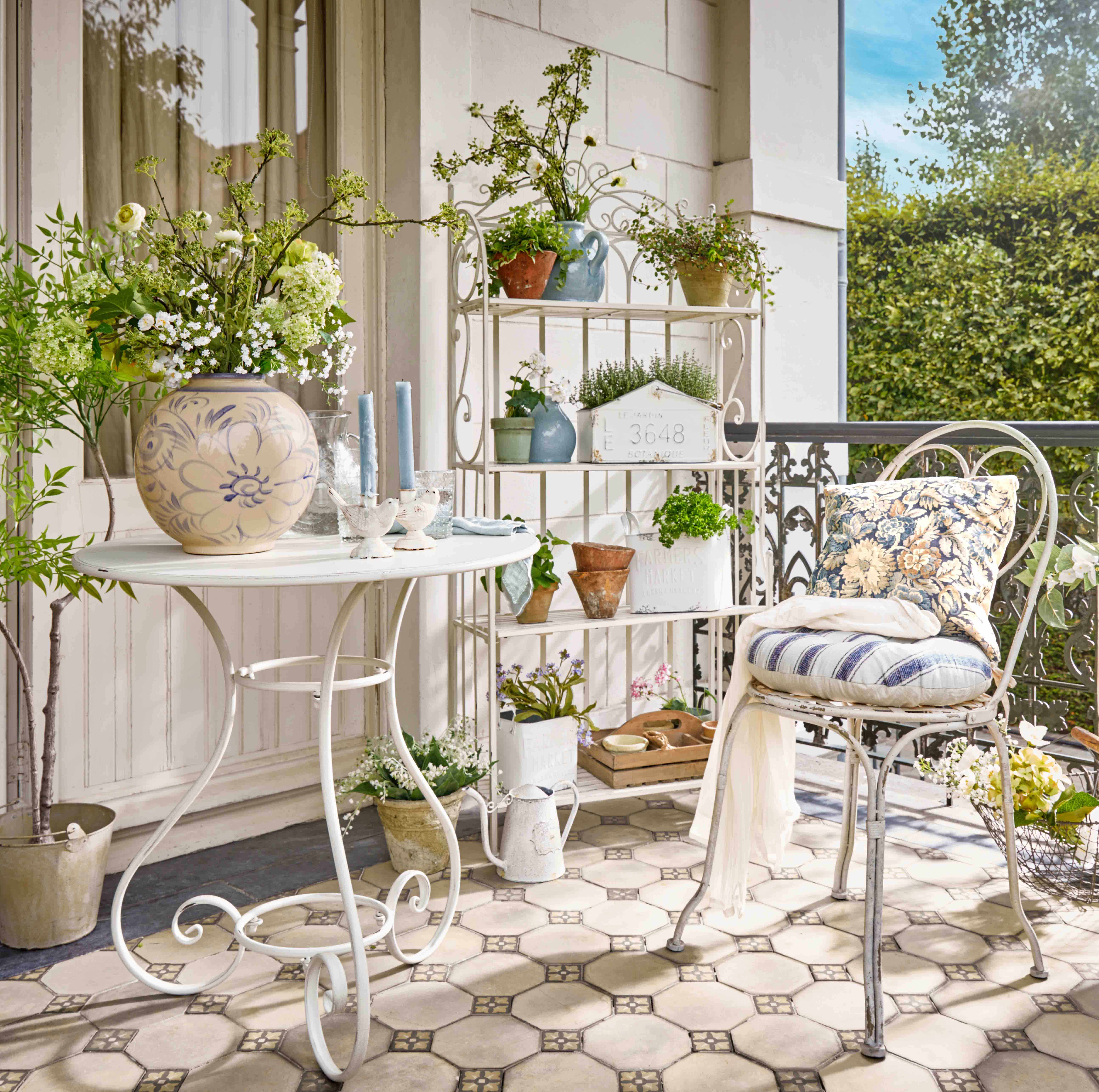 Estantería metálica blanca con plantas en macetas y velas decorativas en terraza con flores