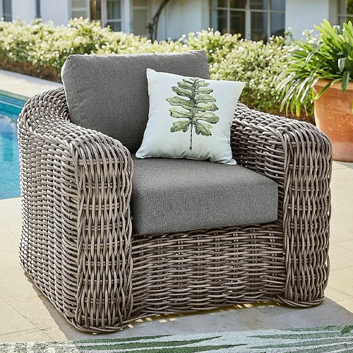 Sillón de jardín de mimbre gris con cojines grises y cojín decorativo con hoja verde