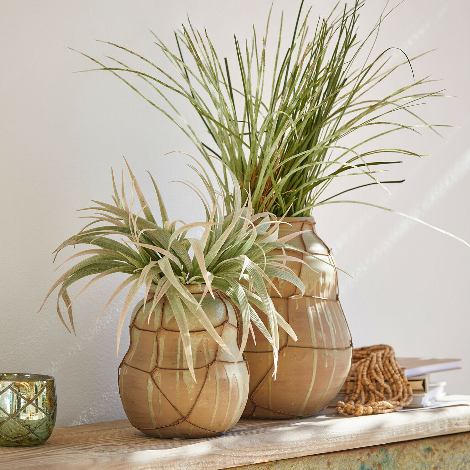 Set de 2 jarrones Frandoro Dos jarrones de cerámica beige con plantas verdes decorativas sobre mesa de madera clara