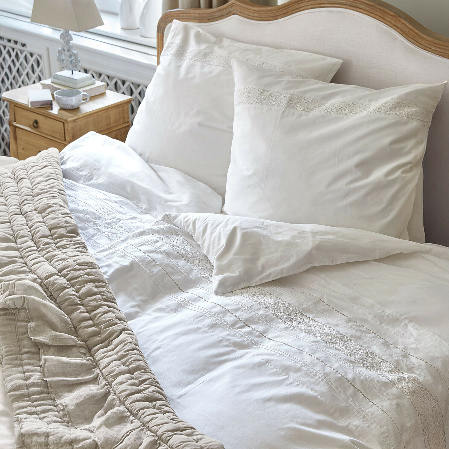 Ropa de cama Isolineas Ropa de cama blanca con encaje sobre cama de madera clara y manta beige