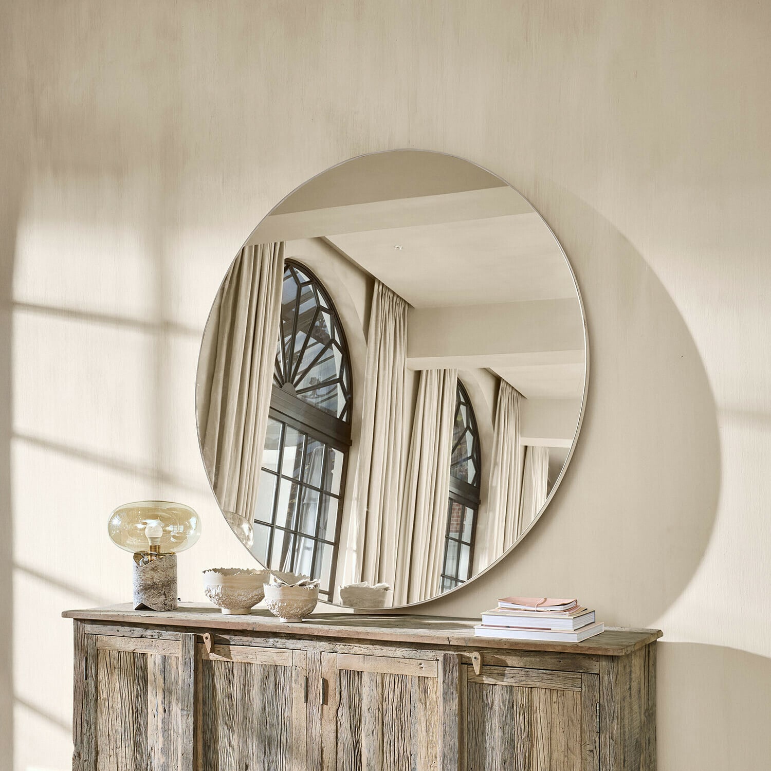 Gran espejo redondo colgado sobre una cómoda de madera en un interior luminoso y natural