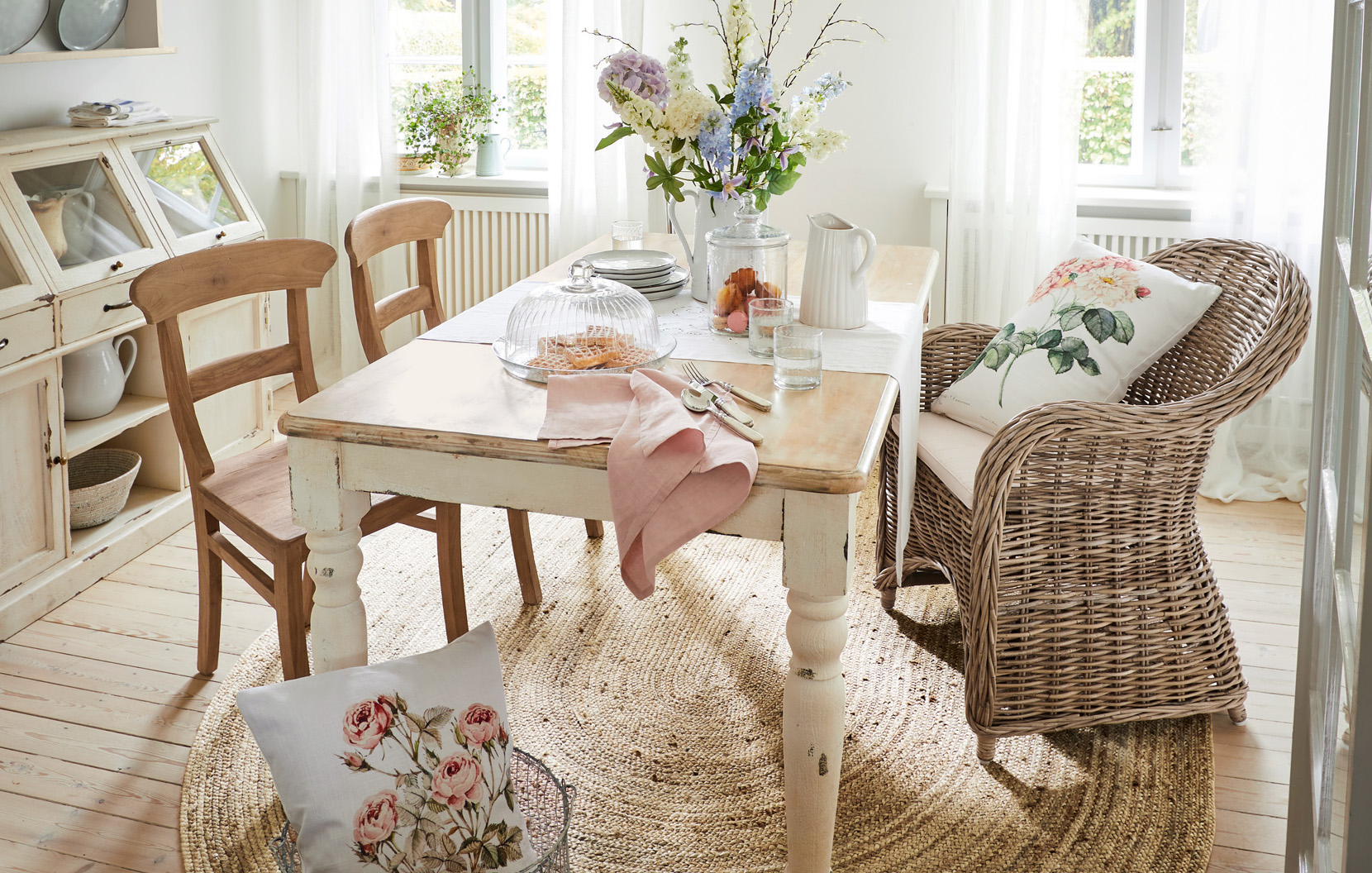 Comedor shabby chic con mesa de madera, sillón de mimbre y decoración floral luminosa