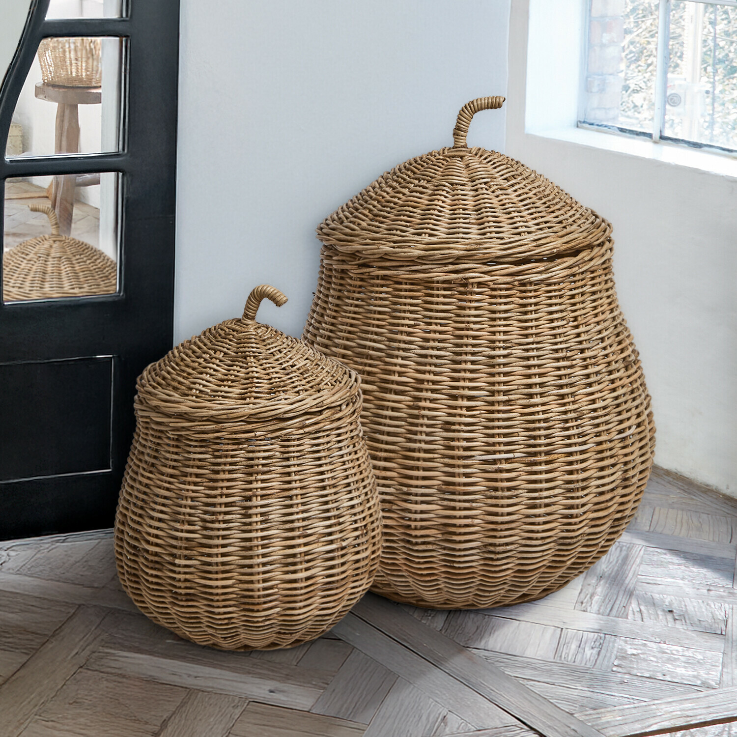 Set de 2 cestas Fernn Dos cestas de mimbre natural con tapa sobre suelo de madera junto a ventana, decoración interior