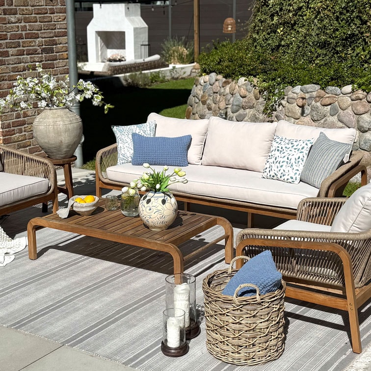 Conjunto de muebles de jardín de madera con sofá beige y cojines azules estampados sobre alfombra a rayas