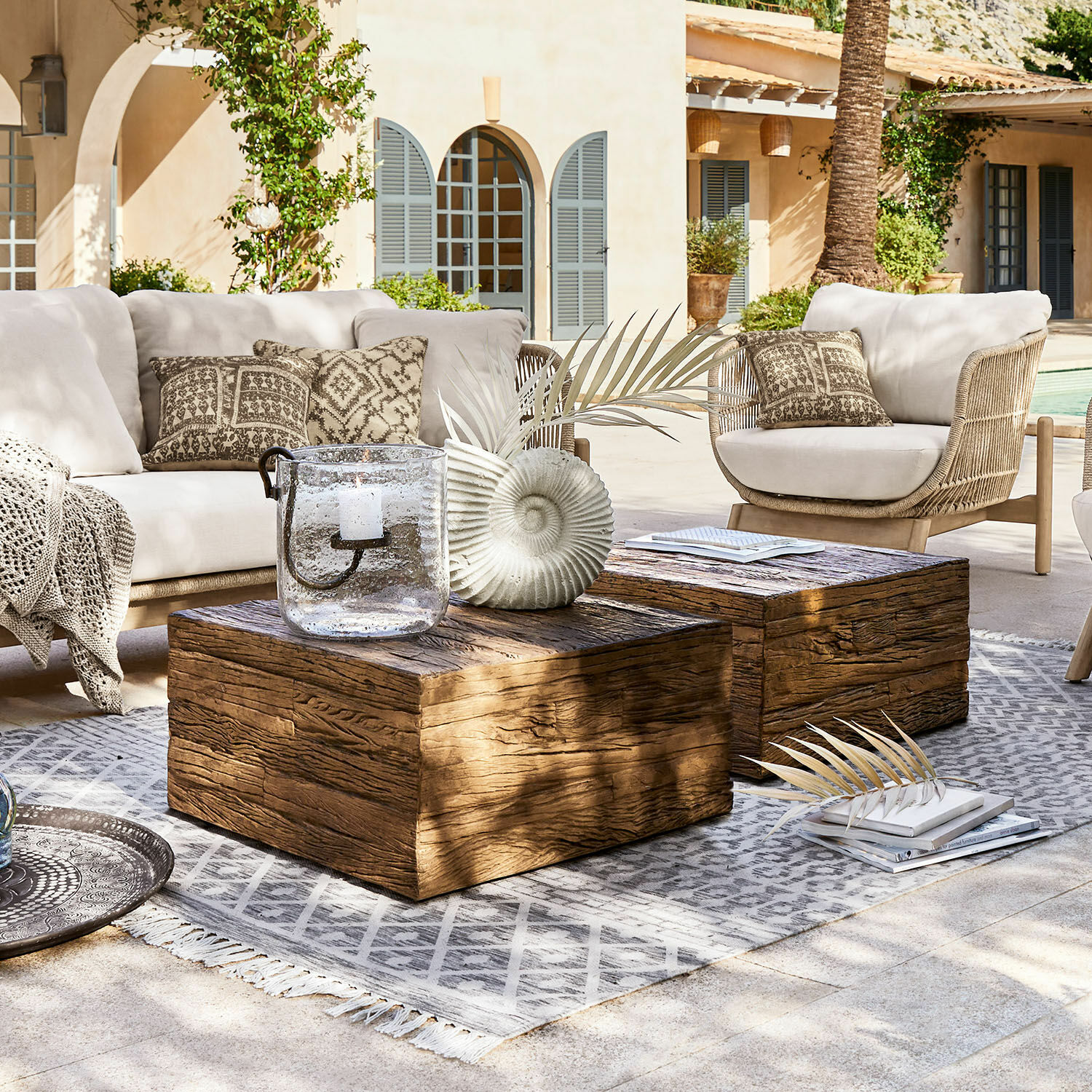 Mesa de centro Glâne Conjunto de muebles de jardín con cojines claros y mesas de madera sobre alfombra gris en terraza