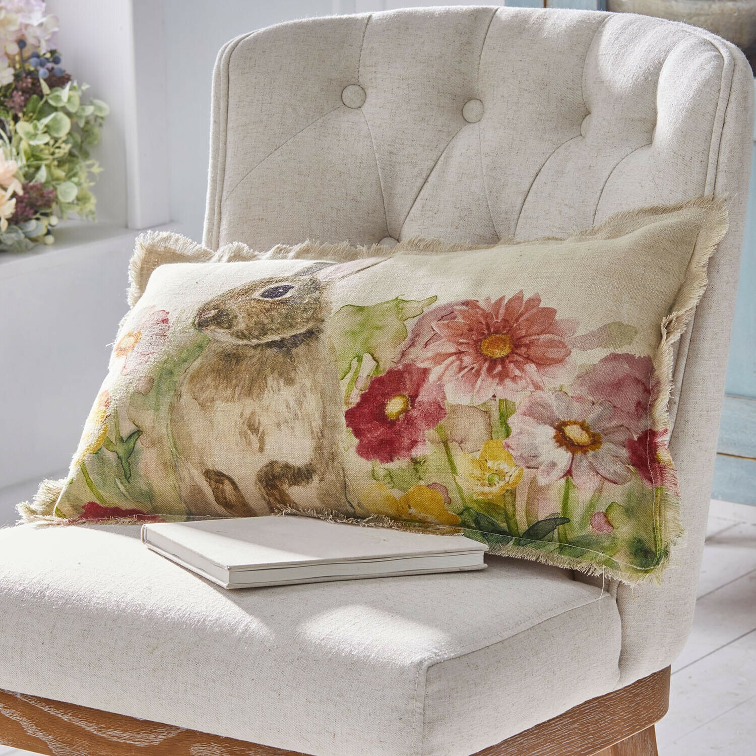 Funda de cojín Parélys Cojín rectangular de lino con diseño de conejo y flores en colores pastel sobre silla clara