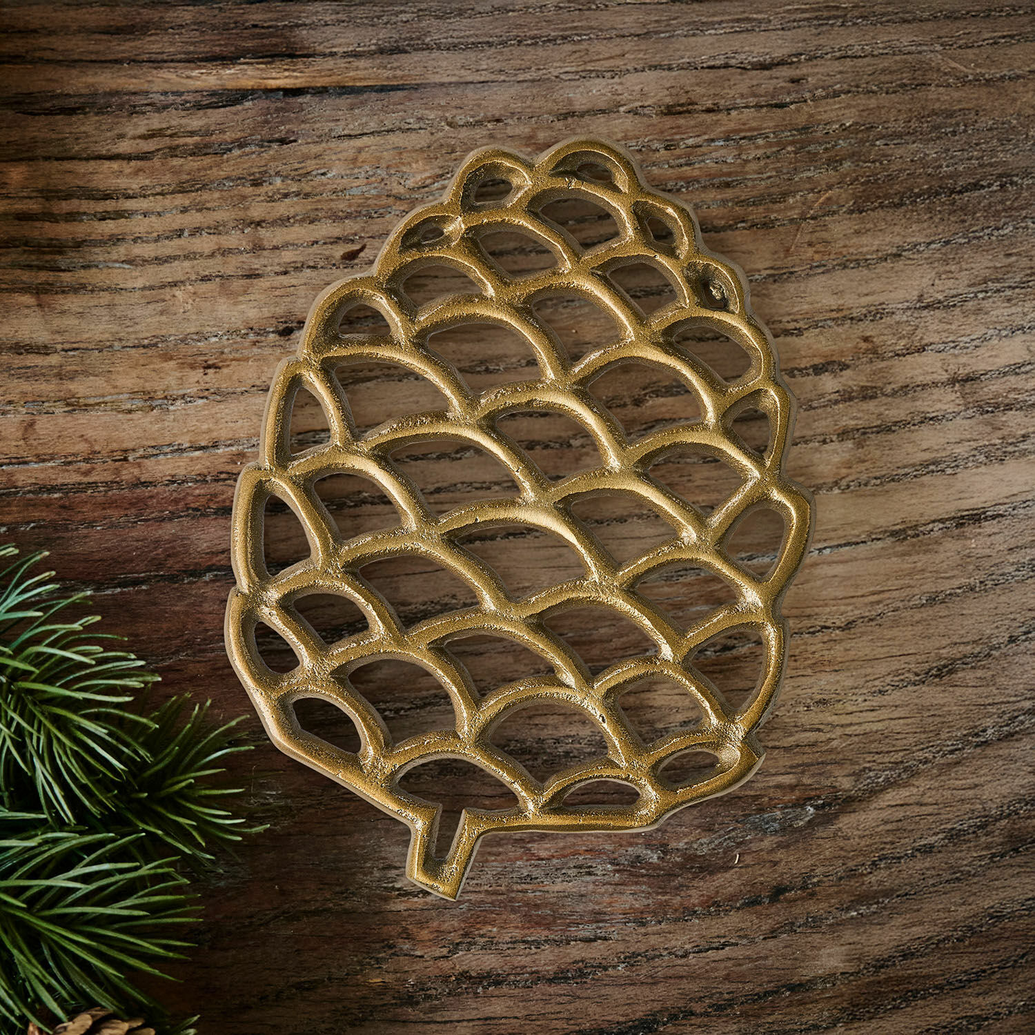 Salvamanteles Caritha Posavasos metálico dorado con forma de piña sobre mesa de madera con ramas verdes