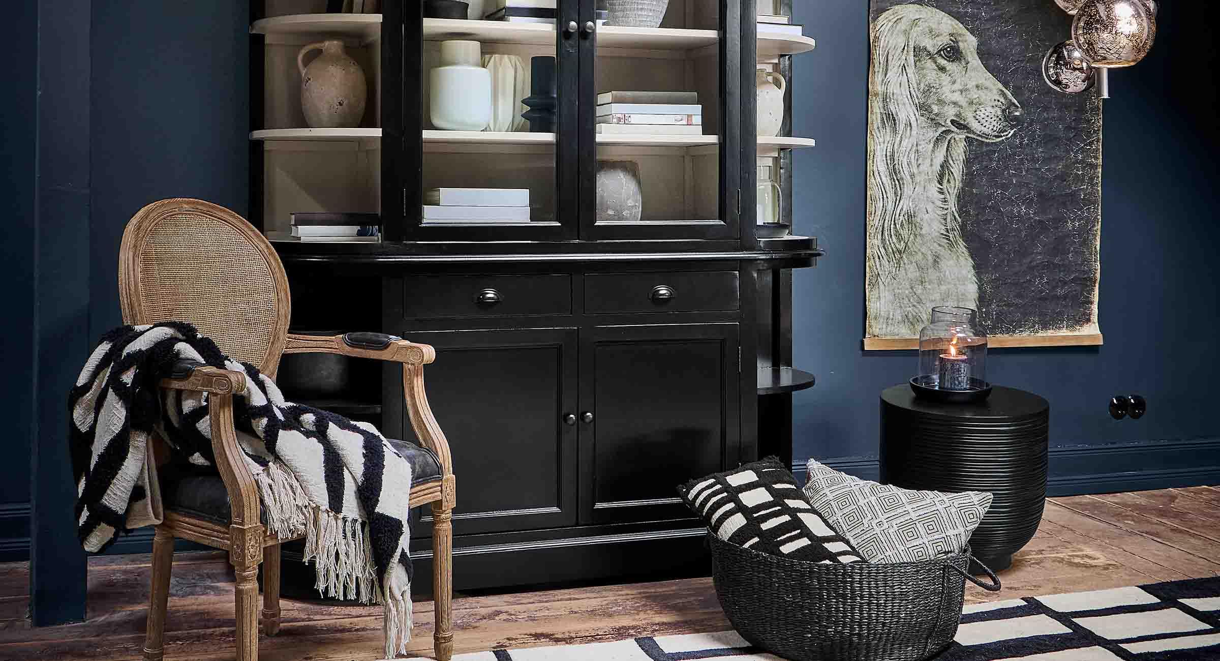 Vitrina negra de madera con estantes, decoraciones naturales y sillón de mimbre en salón moderno