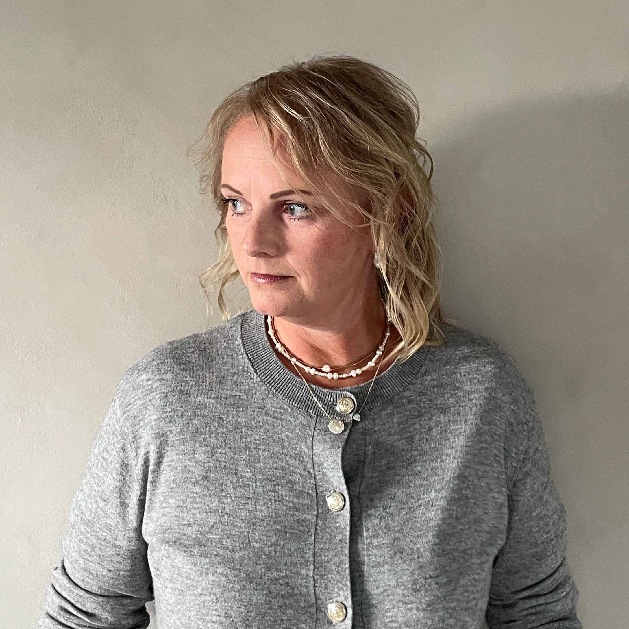 Mujer con cárdigan gris con botones y collares, estilo casual sobre fondo claro