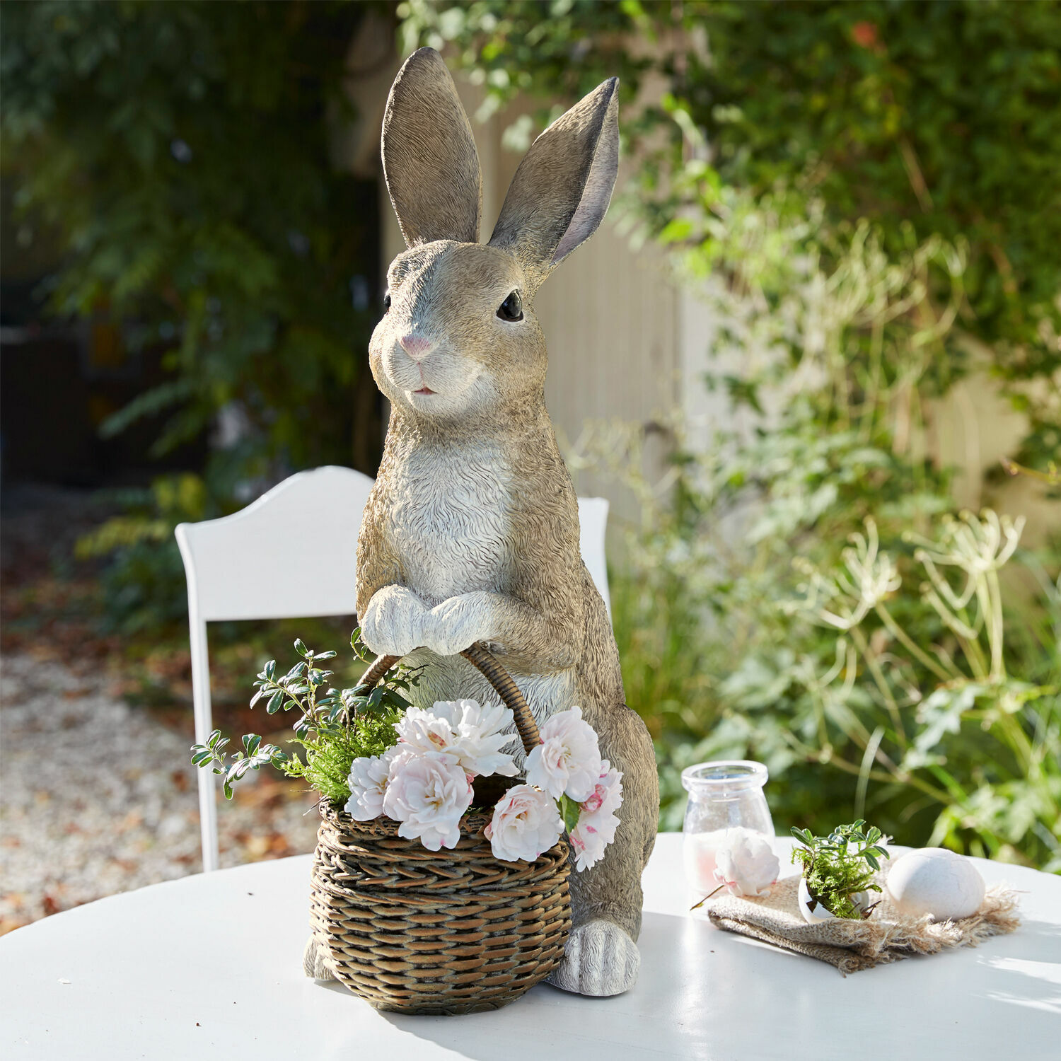 Conejo con cesta para plantas Alais Conejo decorativo de resina con cesta de mimbre y flores blancas en mesa exterior