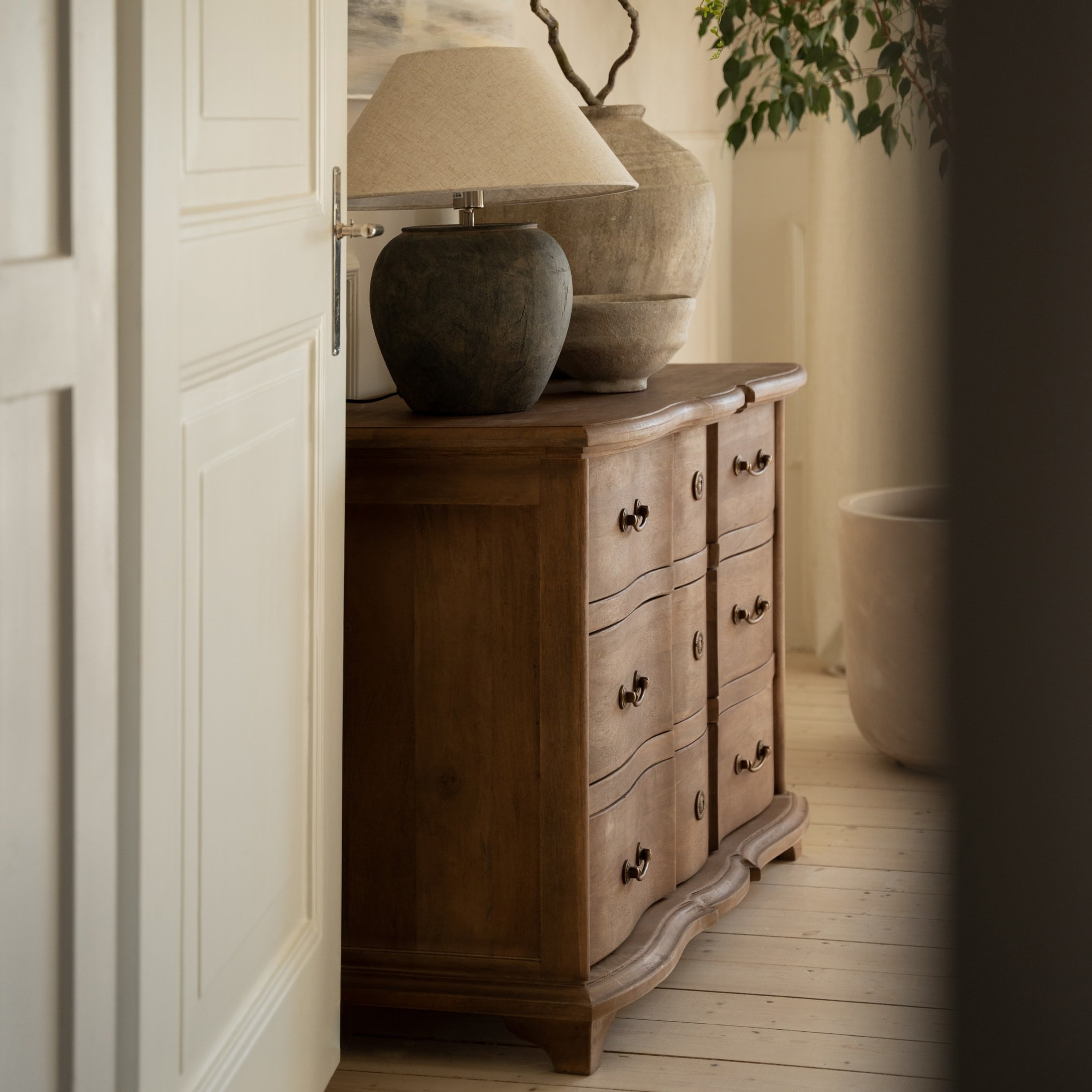 Cómoda de madera con cajones decorativos y lámpara con pantalla beige en interior acogedor