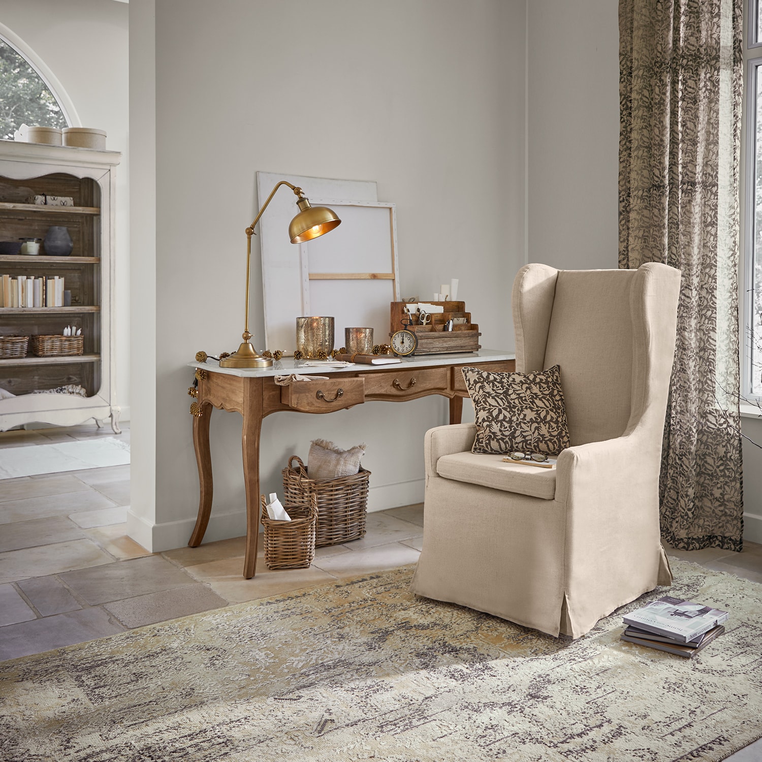 Sillón orejero beige de tela en salón clásico con escritorio de madera y lámpara de mesa