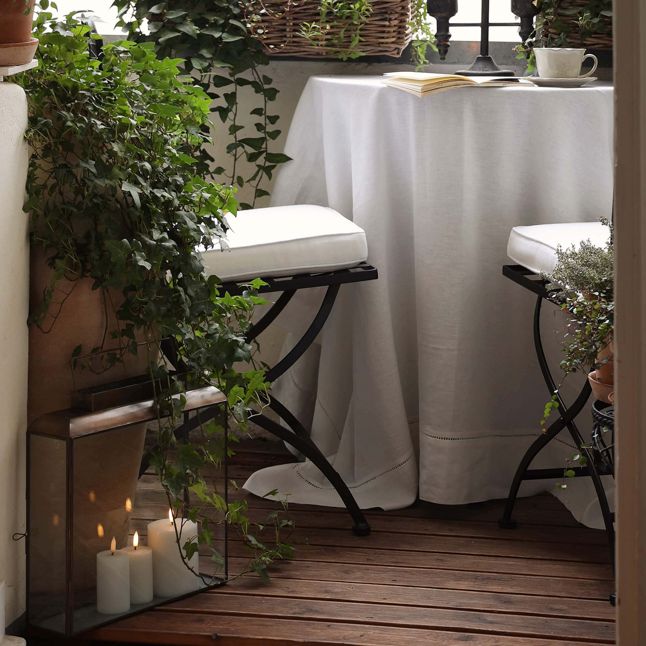 Balcón acogedor con suelo de madera, mantel blanco y sillas metálicas con cojines blancos