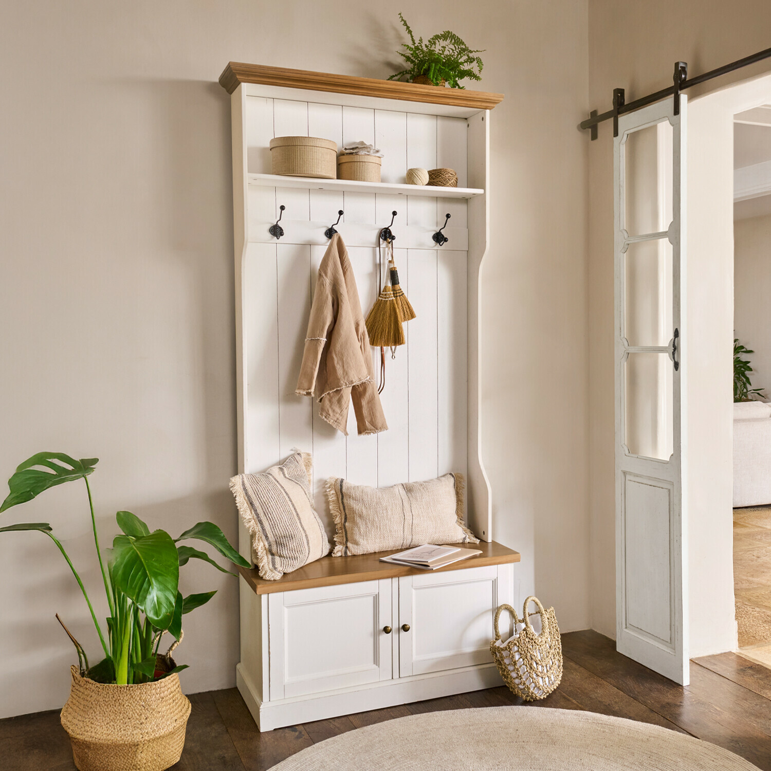 Mueble de entrada blanco de madera con asiento, ganchos, cojines beige y decoración natural con planta
