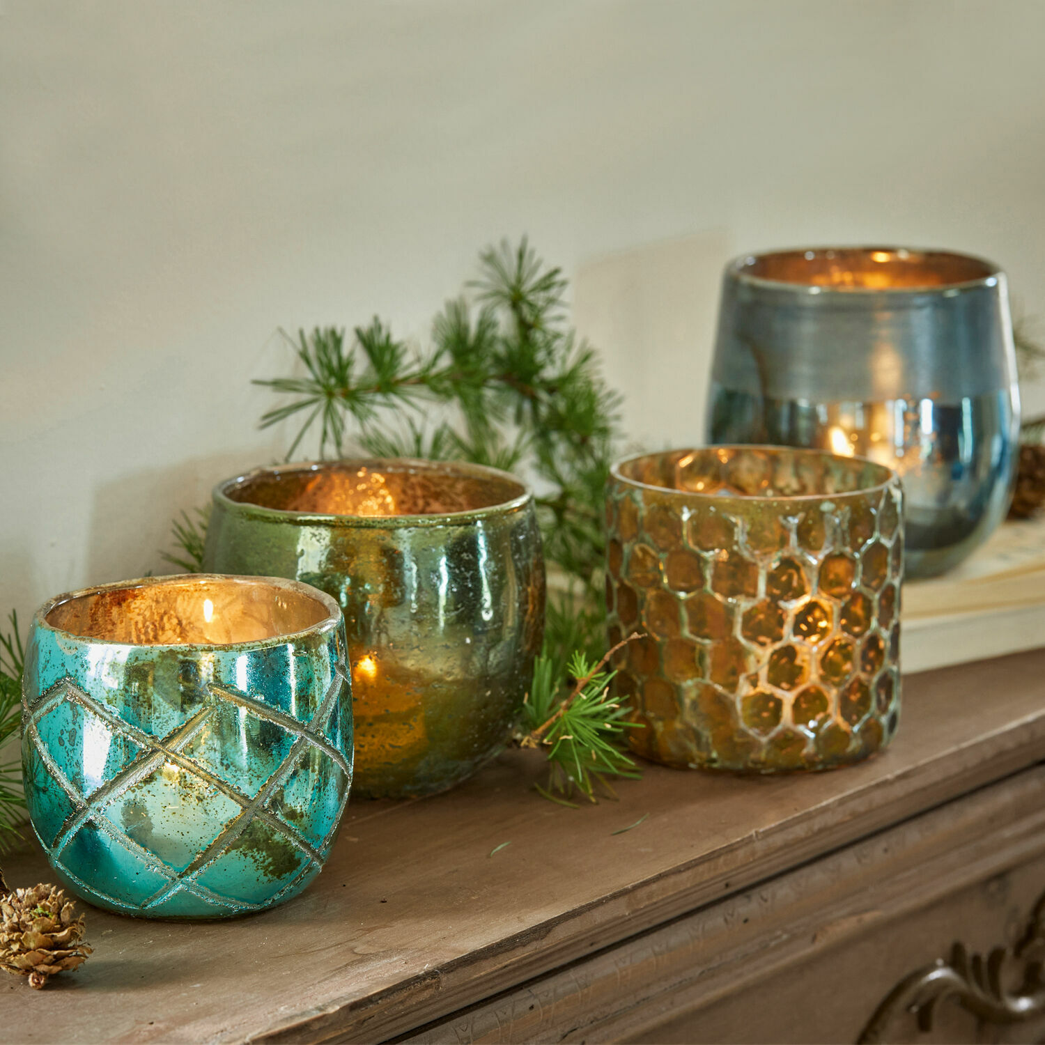 Set de 4 portavelas Marine Conjunto de cuatro portavelas de vidrio en turquesa, verde y dorado sobre una superficie de madera