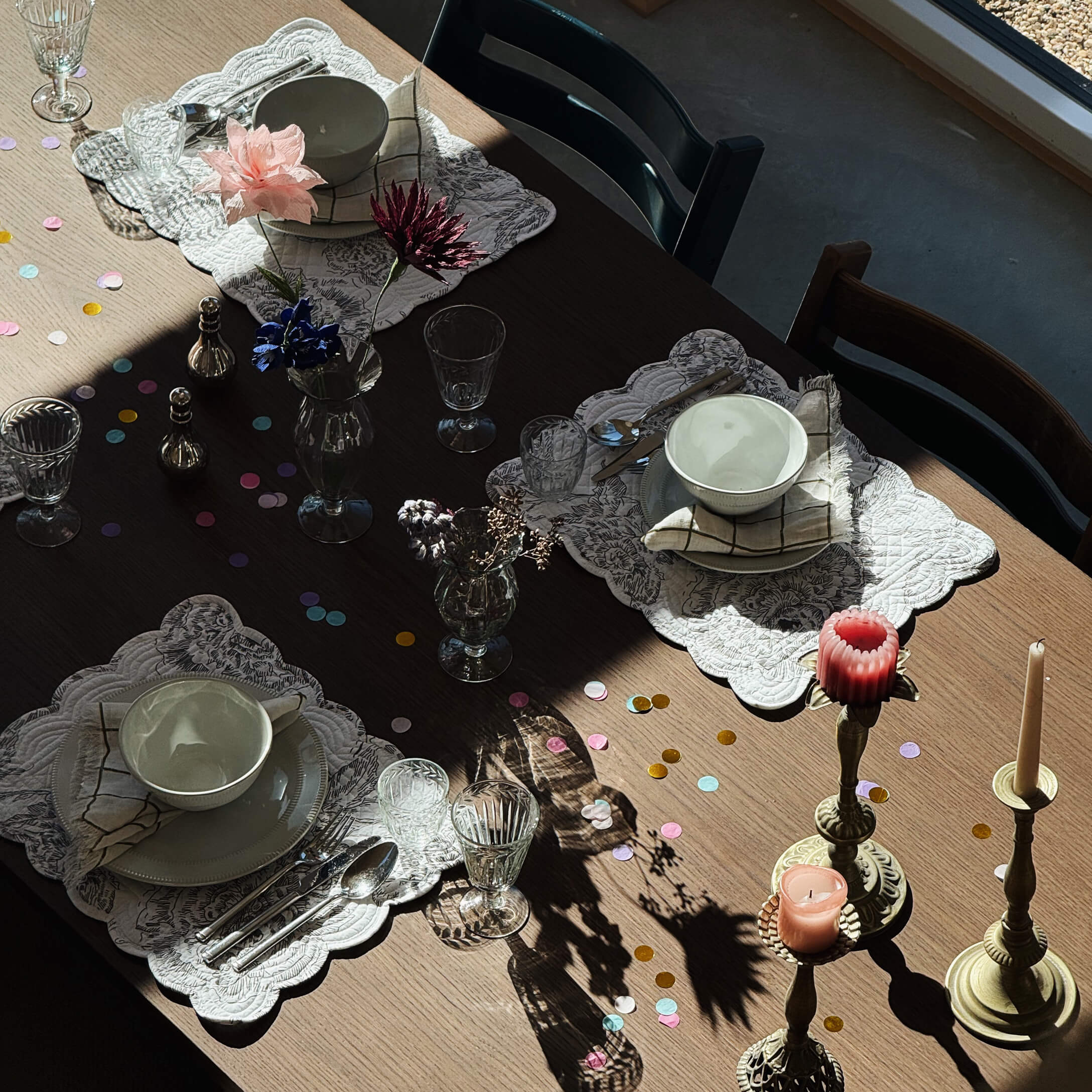 Mesa de madera con cuencos de cerámica blanca, vasos y velas en candelabros de latón