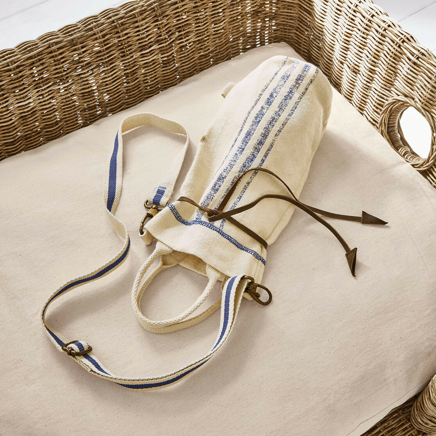 Bolsa portabotellas Pawera Bolsa de algodón beige con rayas azules y cordón de cuero sobre cojín claro con respaldo de mimbre