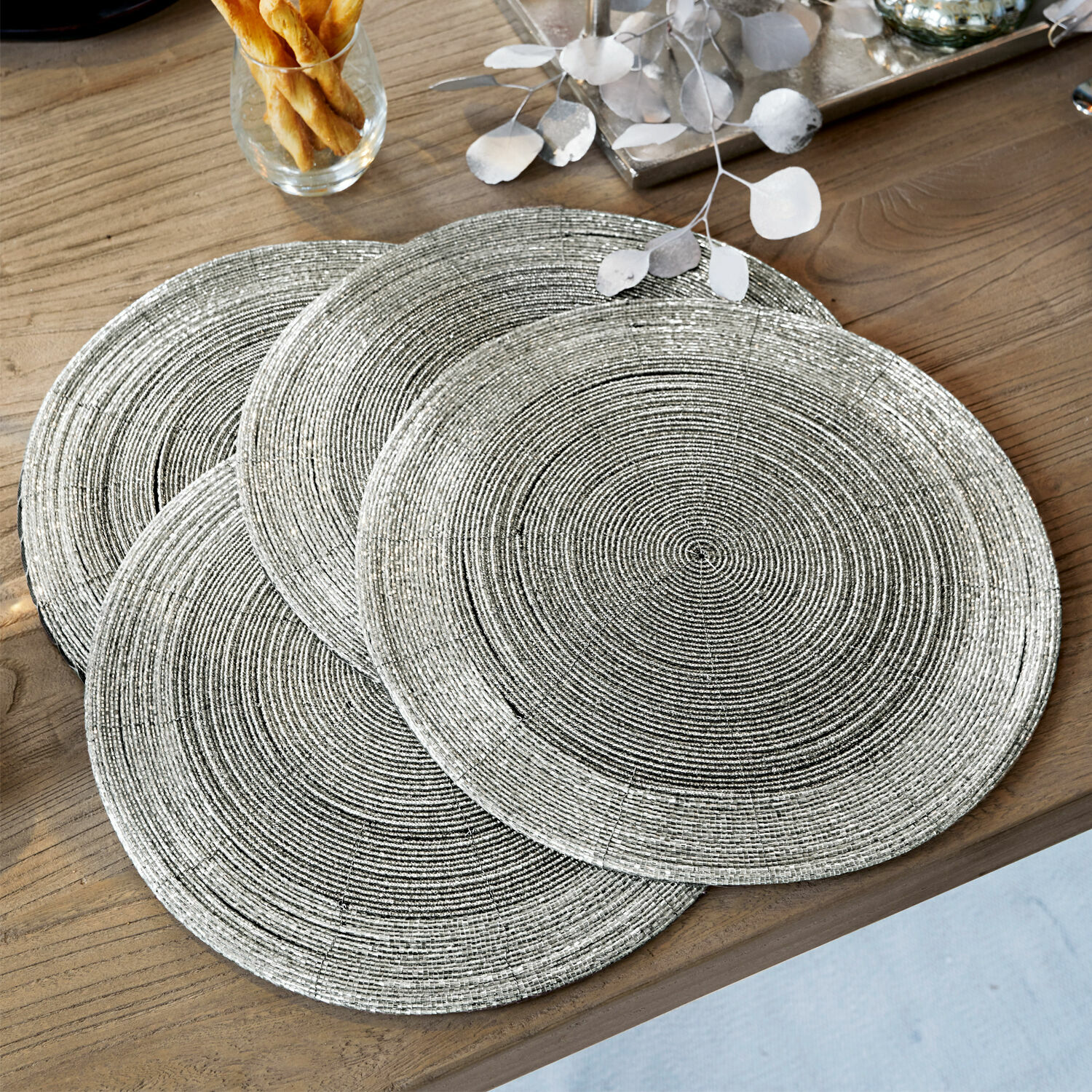 Set de 4 manteles individuales Barningham Juego de cuatro individuales redondos plateados con textura trenzada sobre mesa de madera