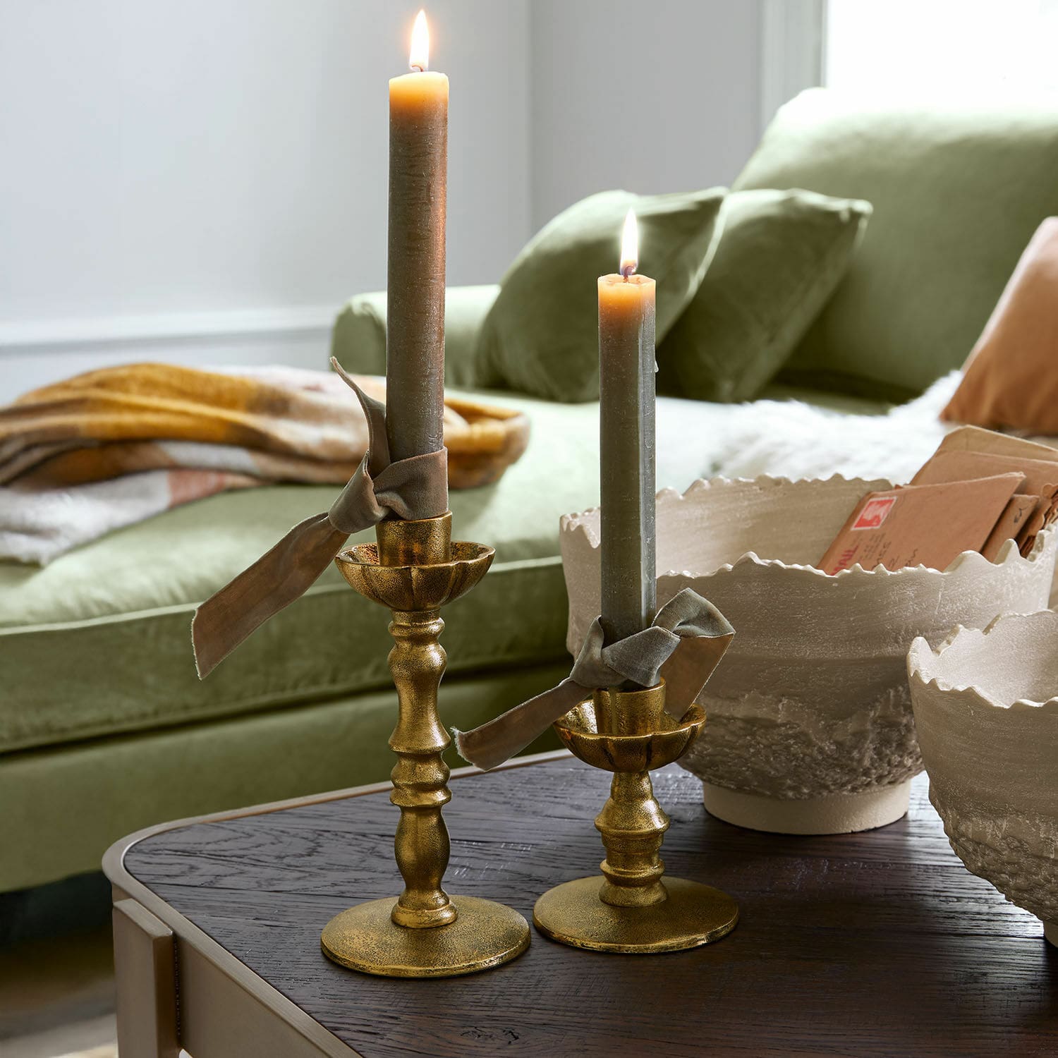 Set de 2 candeleros Zalethar Conjunto de dos candelabros metálicos dorados con velas grises y lazos decorativos sobre mesa de madera