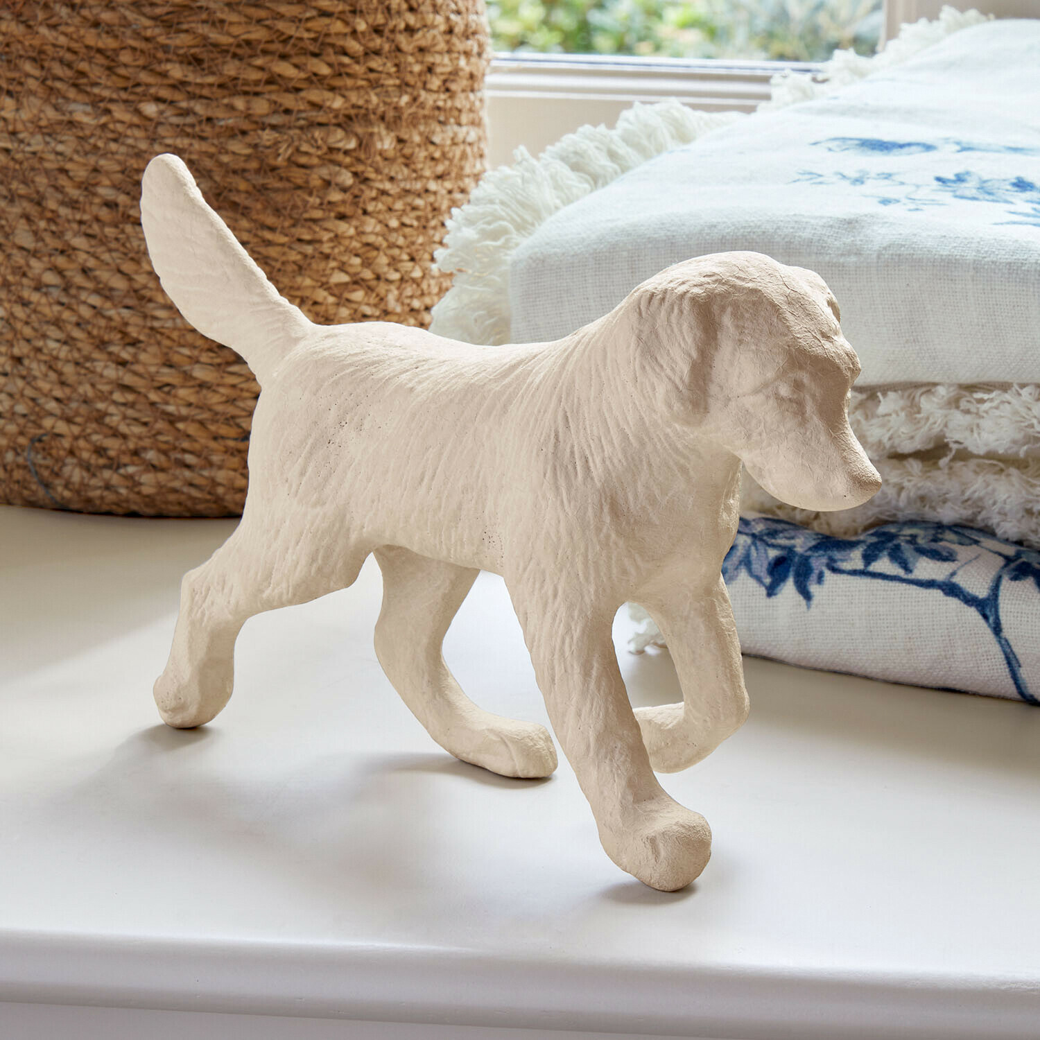 Figura de perro beige con textura de pelaje sobre superficie blanca y tela decorativa al fondo