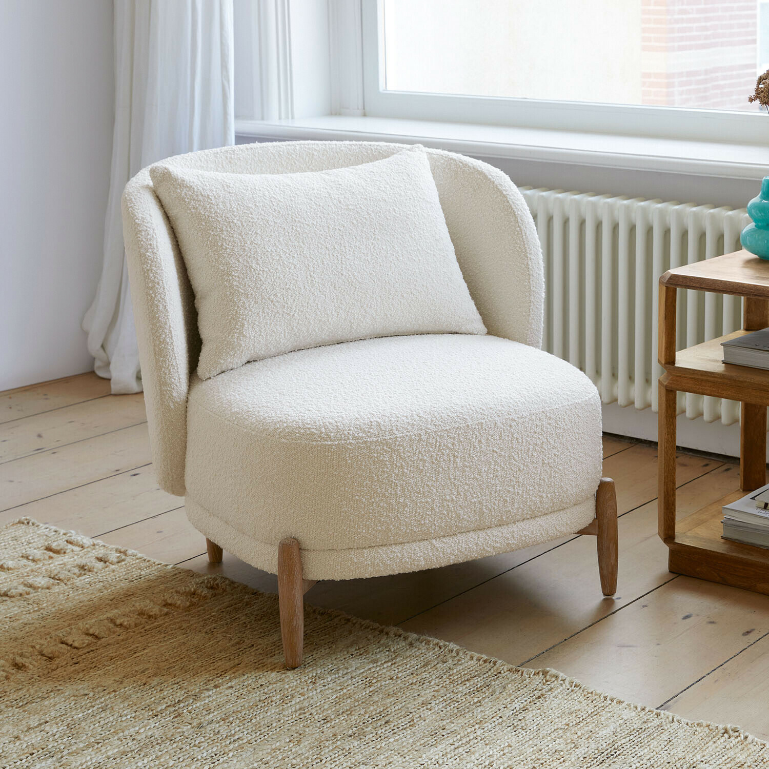 Sillón Thamira Sillón blanco de tela bouclé suave con patas de madera en sala luminosa