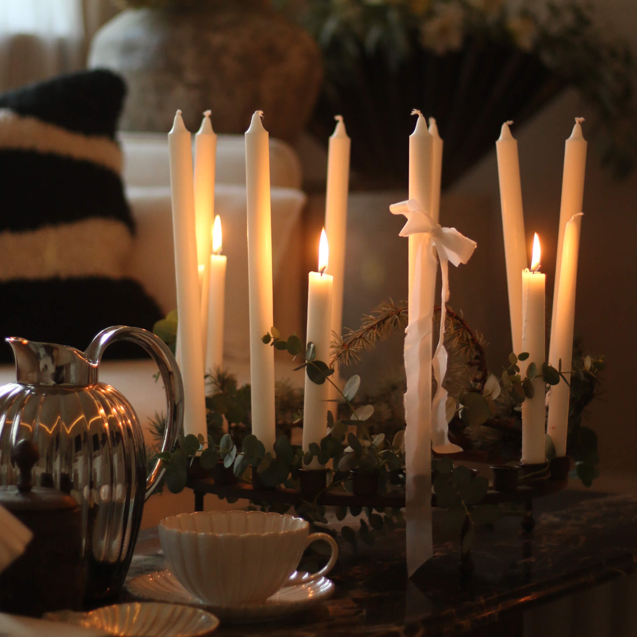Candelabro decorativo con velas blancas y hojas verdes sobre mesa en ambiente acogedor