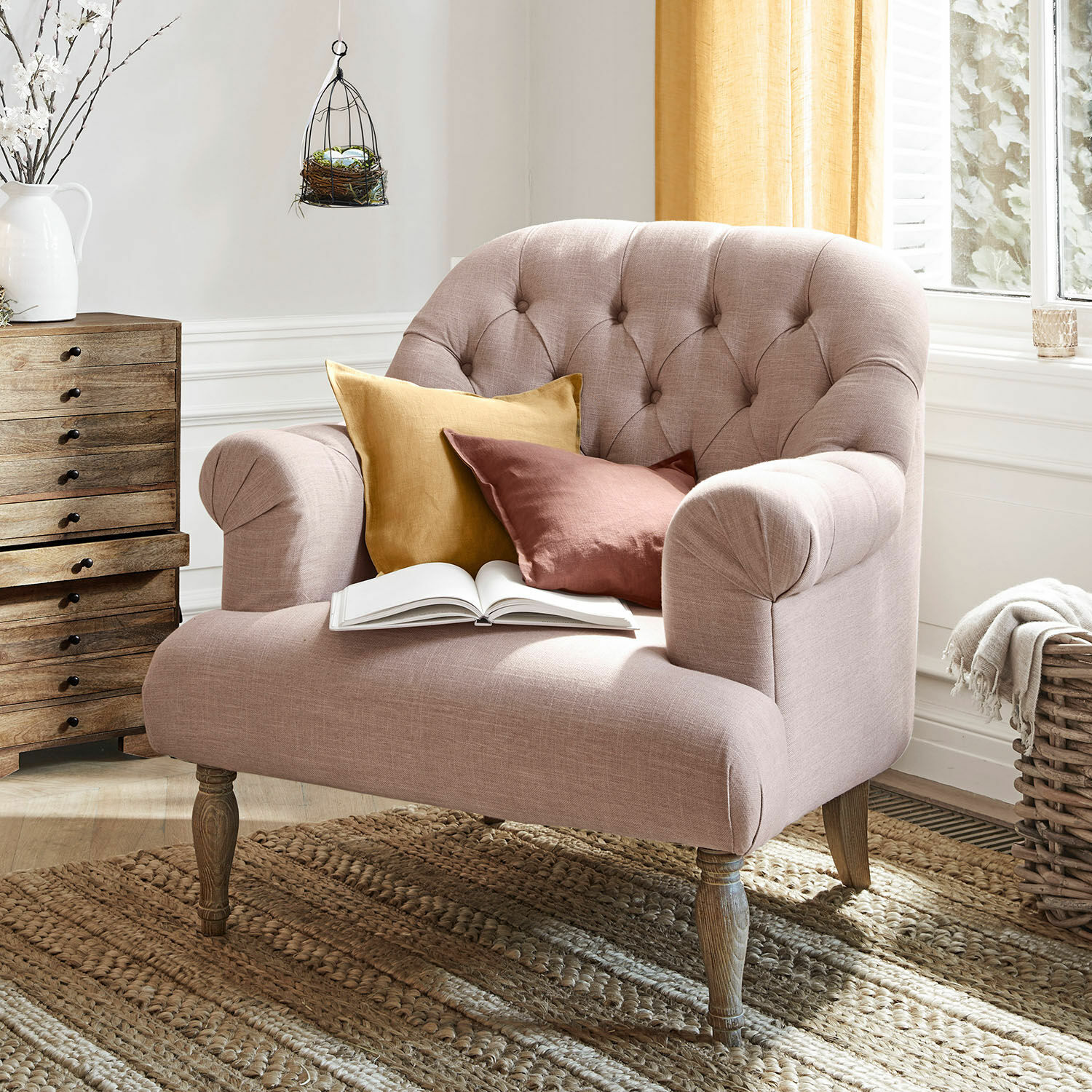 Sillón Shambrook Sofá tapizado rosa con patas de madera y dos cojines en tonos cálidos sobre alfombra tejida