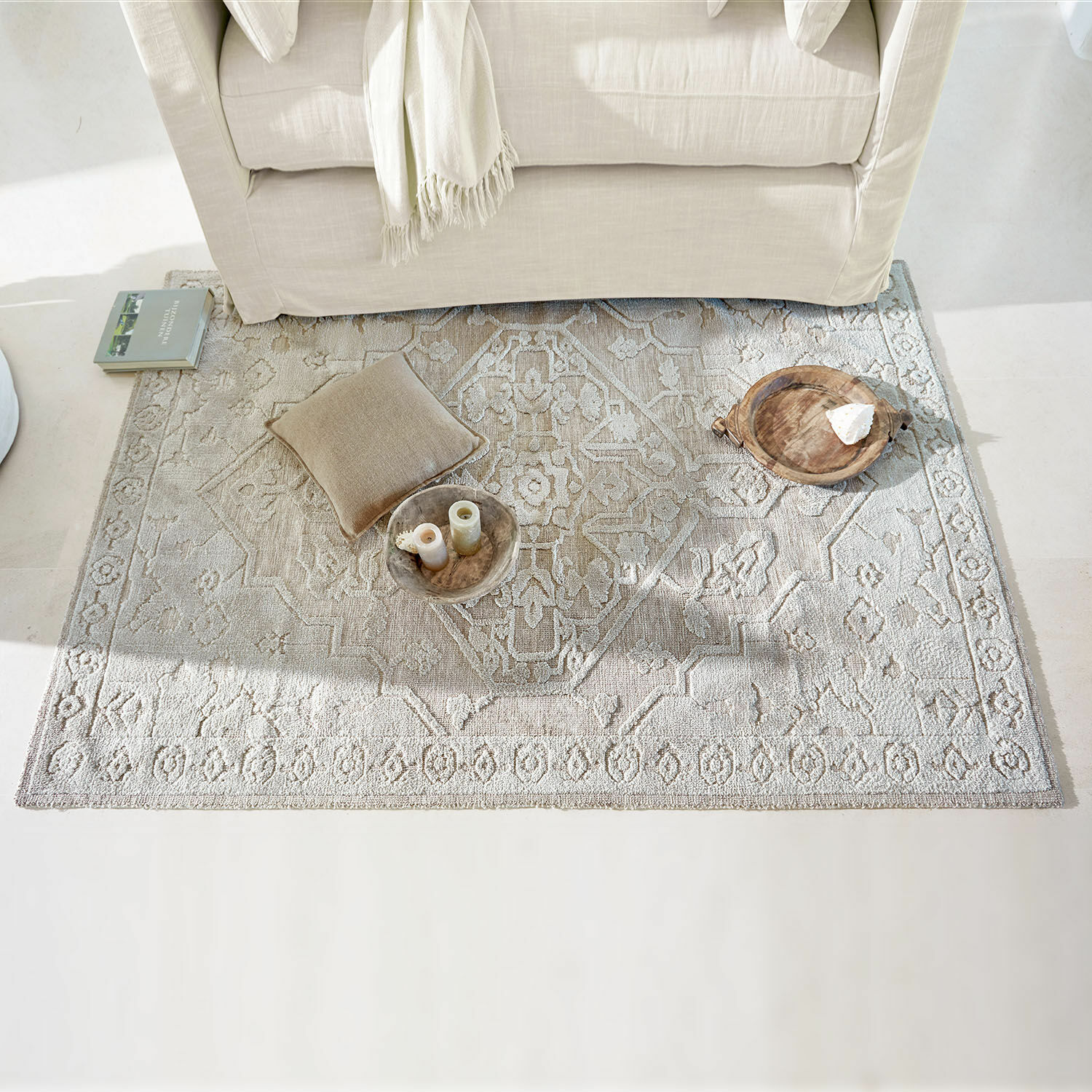 Alfombra Armidale Alfombra beige con patrón delicado bajo un sofá claro, cojín y decoraciones en el suelo