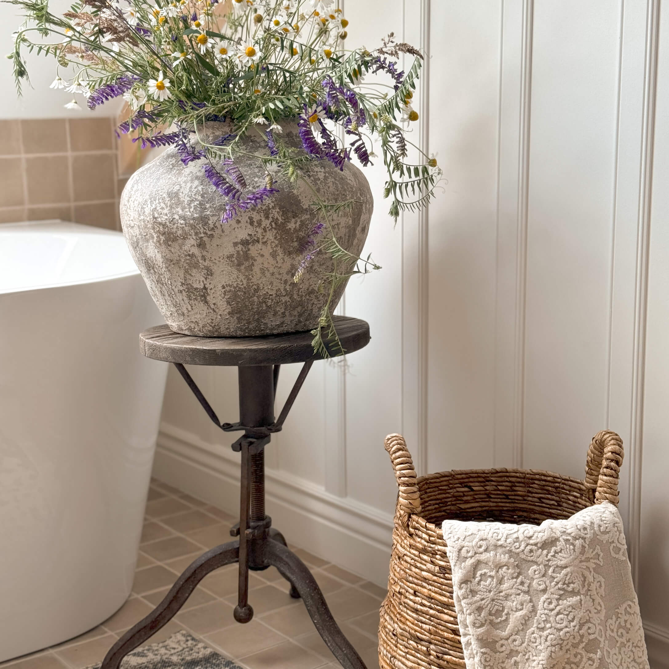 Jarrón rústico de piedra gris con flores silvestres sobre soporte metálico en baño