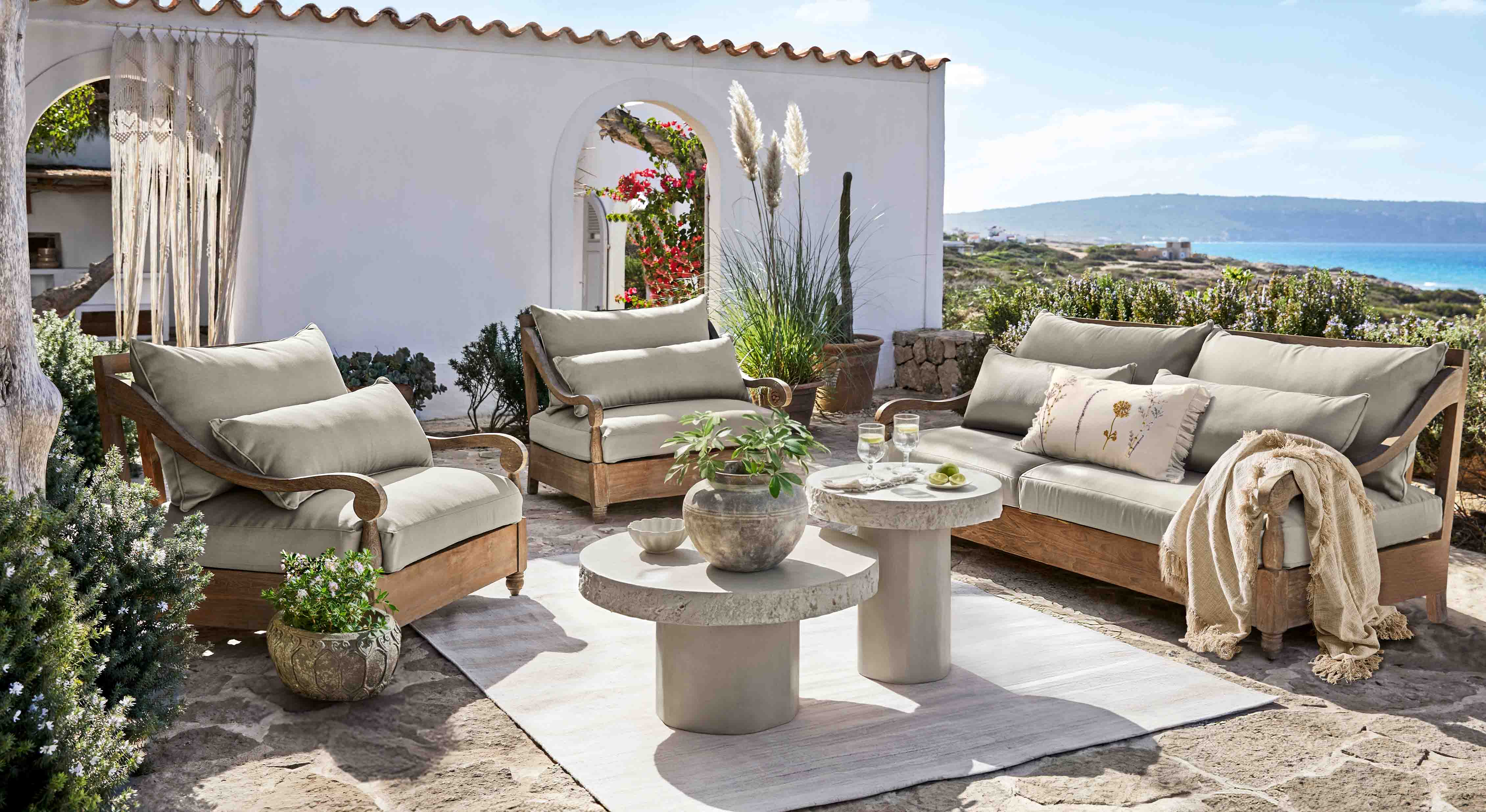 Conjunto de muebles de jardín de madera con cojines grises en terraza con vistas al mar