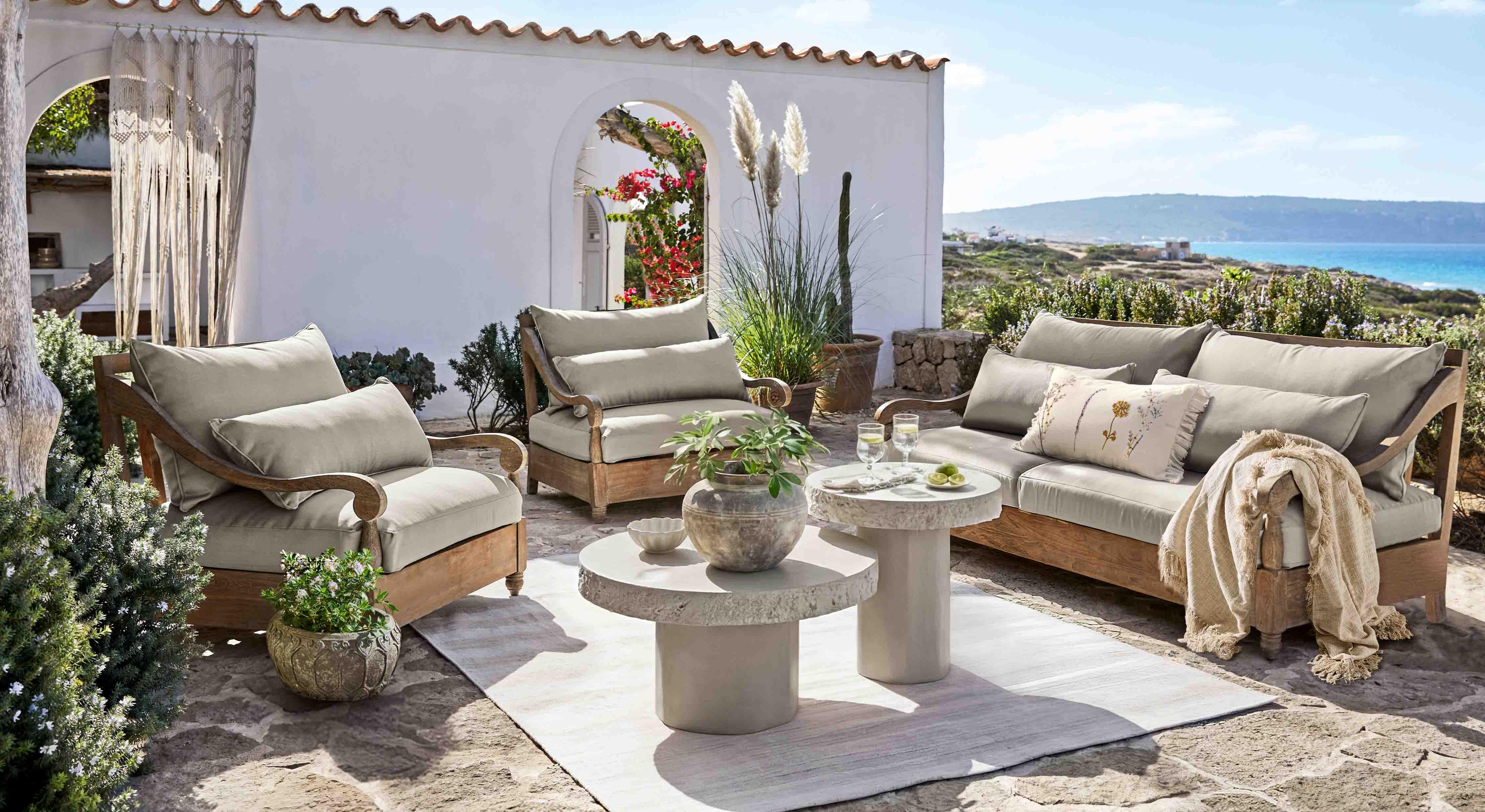 Conjunto de muebles de jardín de madera con cojines grises en terraza con vistas al mar