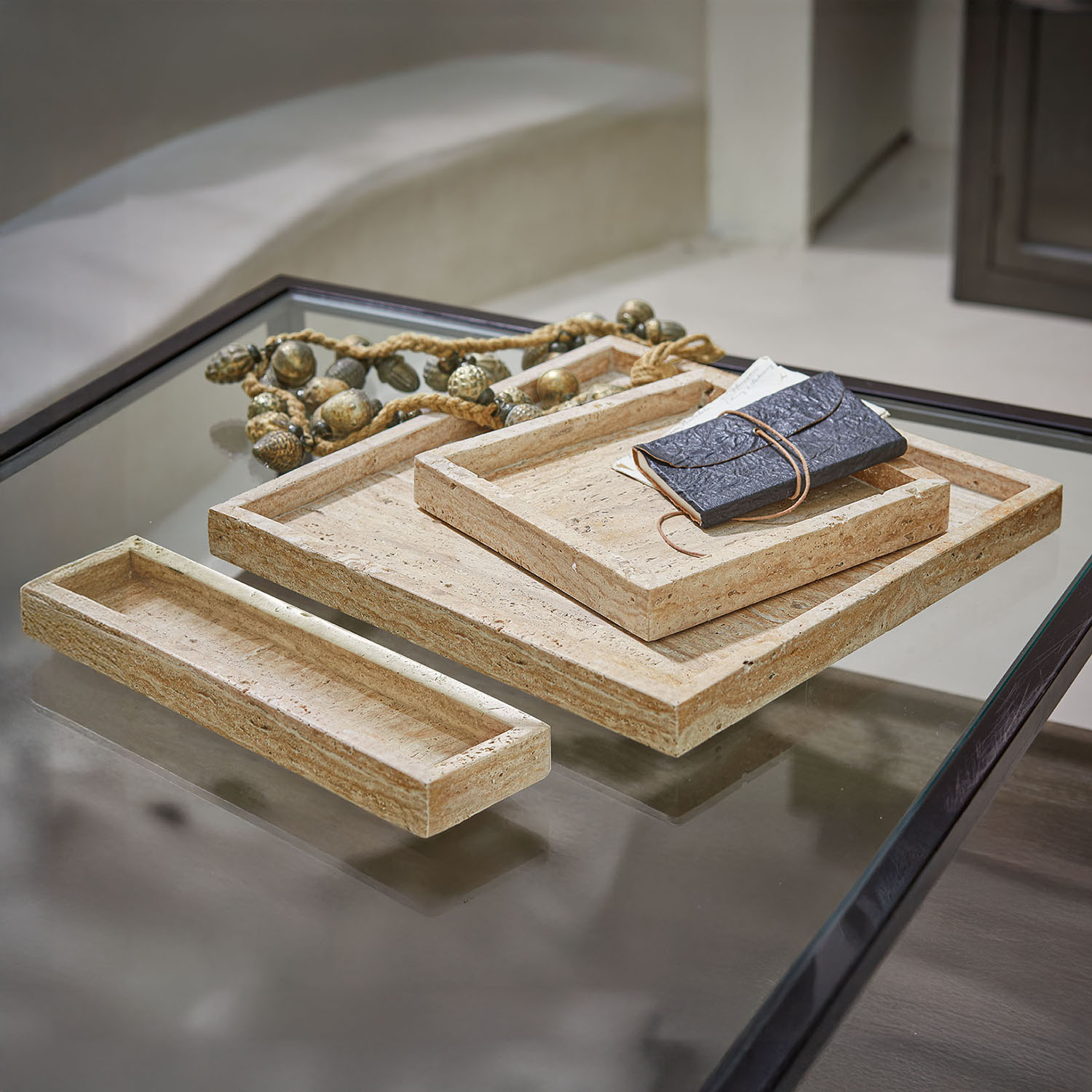 Conjunto de tres bandejas rectangulares de piedra beige sobre mesa de cristal con marco negro
