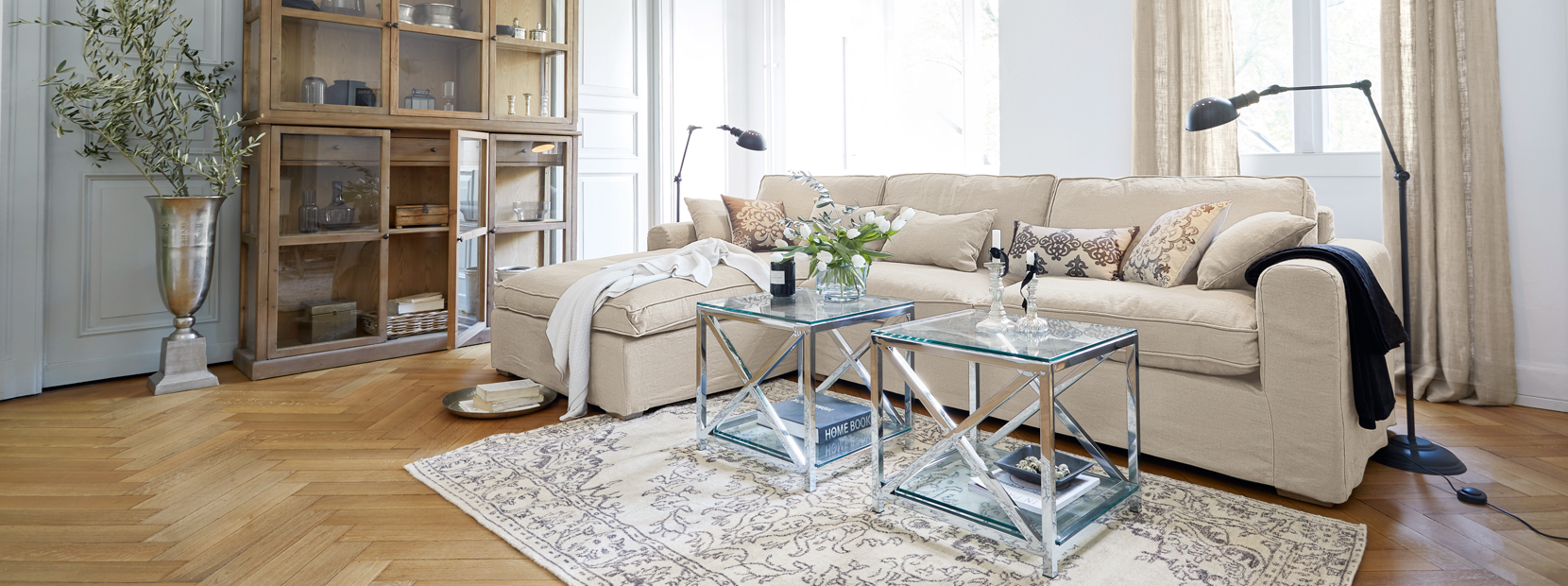 Salón clásico elegante con sofá beige, mesas de cristal y vitrina de madera sobre suelo claro